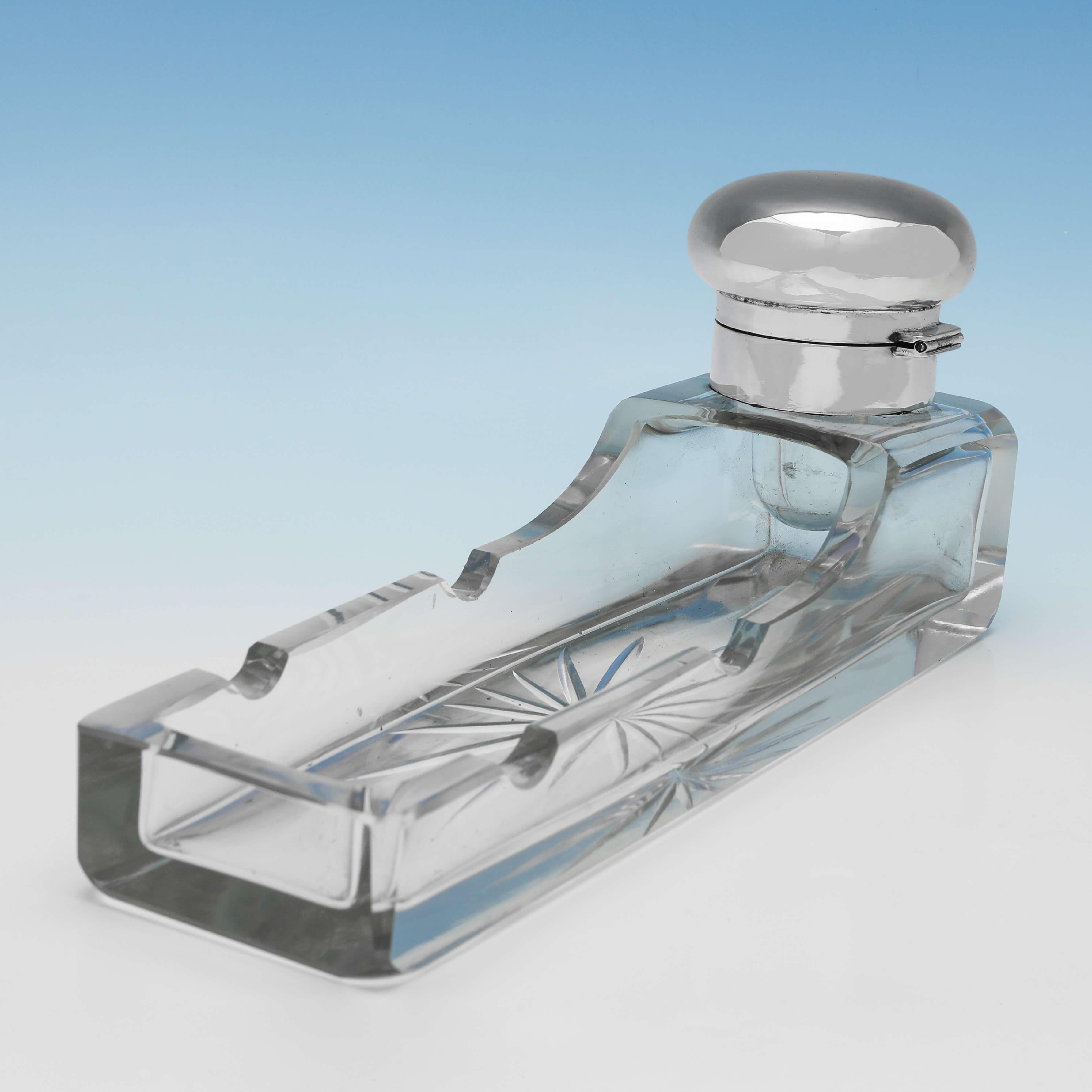 Hallmarked in London in 1913 by Stuart Clifford & Co., this very stylish, Antique Sterling Silver Ink Stand, features an elongated glass body with two pen holders, and a plain silver lid and mount. The ink stand measures 4