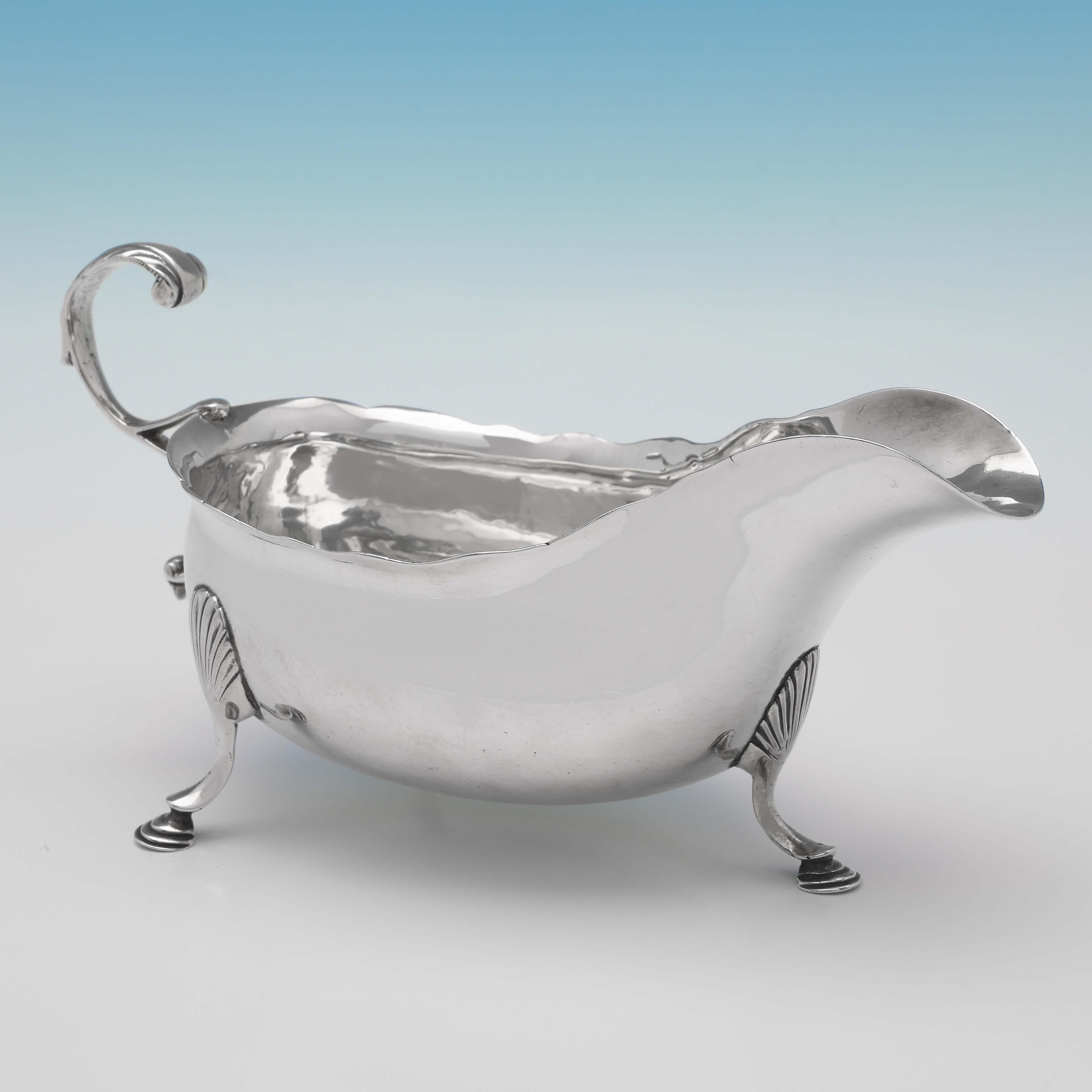 Made in Dublin circa 1780, this handsome, antique sterling silver sauce boat, is plain in style, featuring a scalloped border, an acanthus detailed flying C-scroll handle, and standing on three feet. The sauce boat measures 4