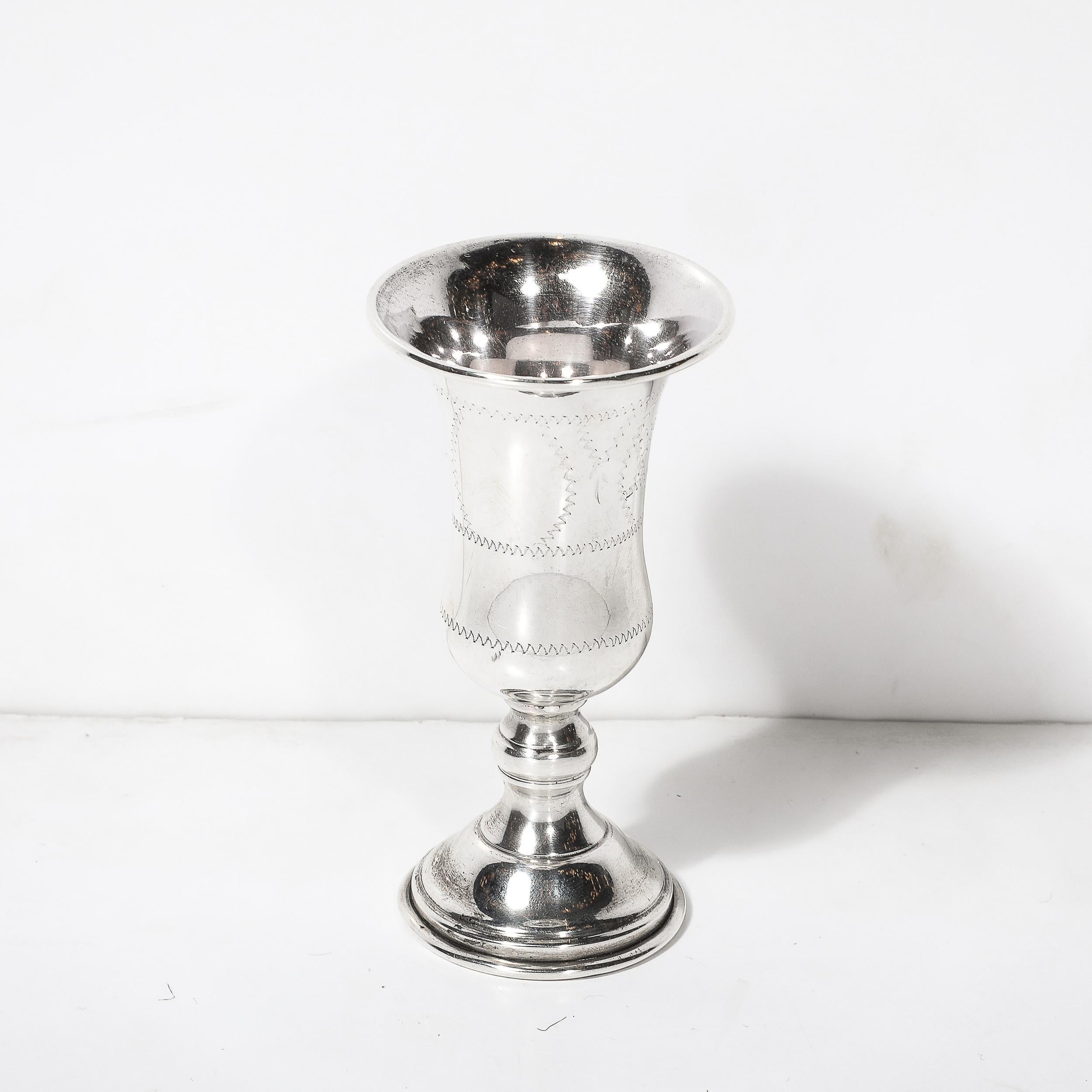 Esta elegante copa de Kiddush de plata de ley, fabricada en América hacia 1960, presenta refinados detalles lineales cincelados a mano y un sutil motivo de la Estrella de David. El diseño, cuidadosamente integrado, equilibra el simbolismo cultural
