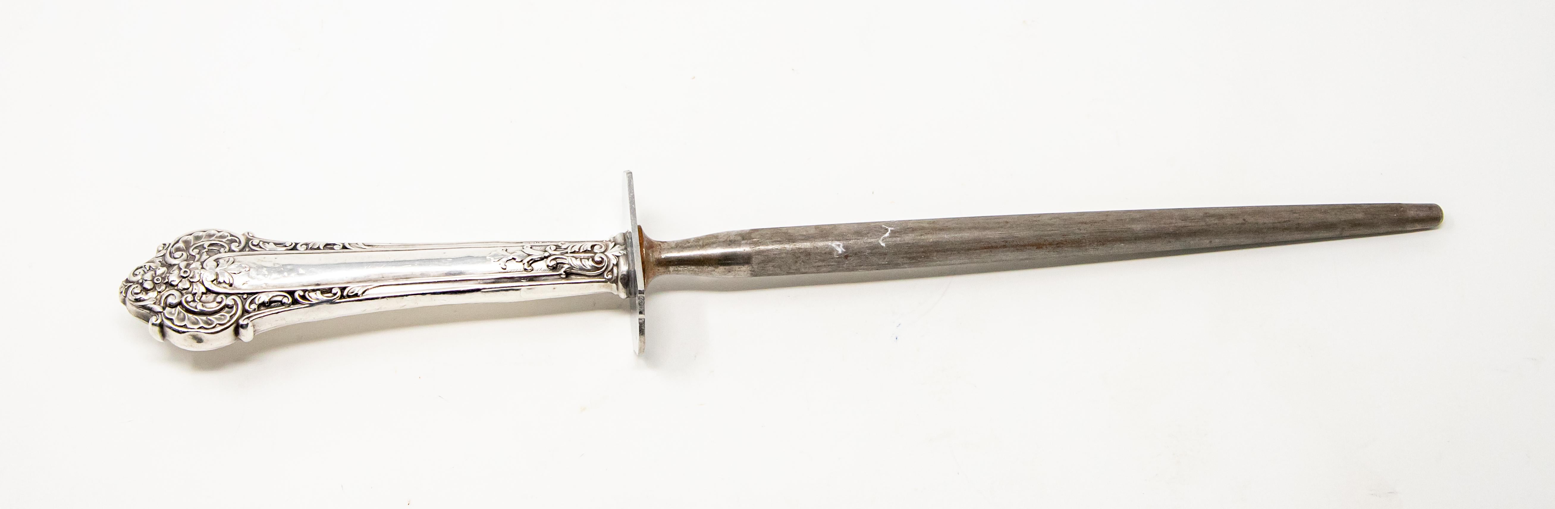 Offering this sterling silver knife sharpener. Having a sterling handle with scrollwork and foliate detail. Hallmarked on the guard sterling handle, with an A in the middle.