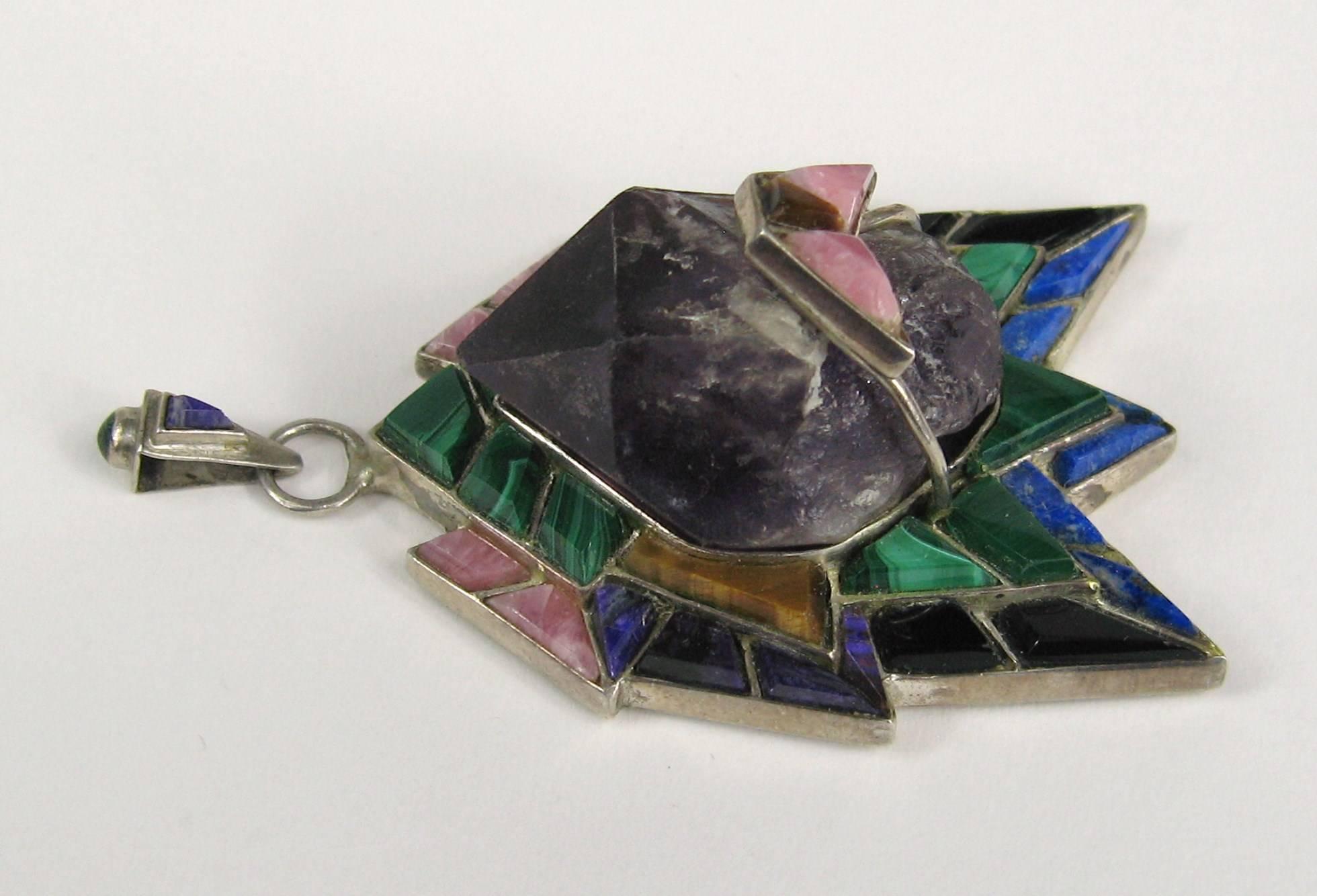 This is a large Hand Crafted Multi-Gemstone Pendant set in sterling silver. There is a large Amethyst Piece in the center surrounded by Malachite, Tigers Eye, Rose Quartz, Onyx, and Lapis. Bale has a cabochon malachite and a bezel set Amethyst in