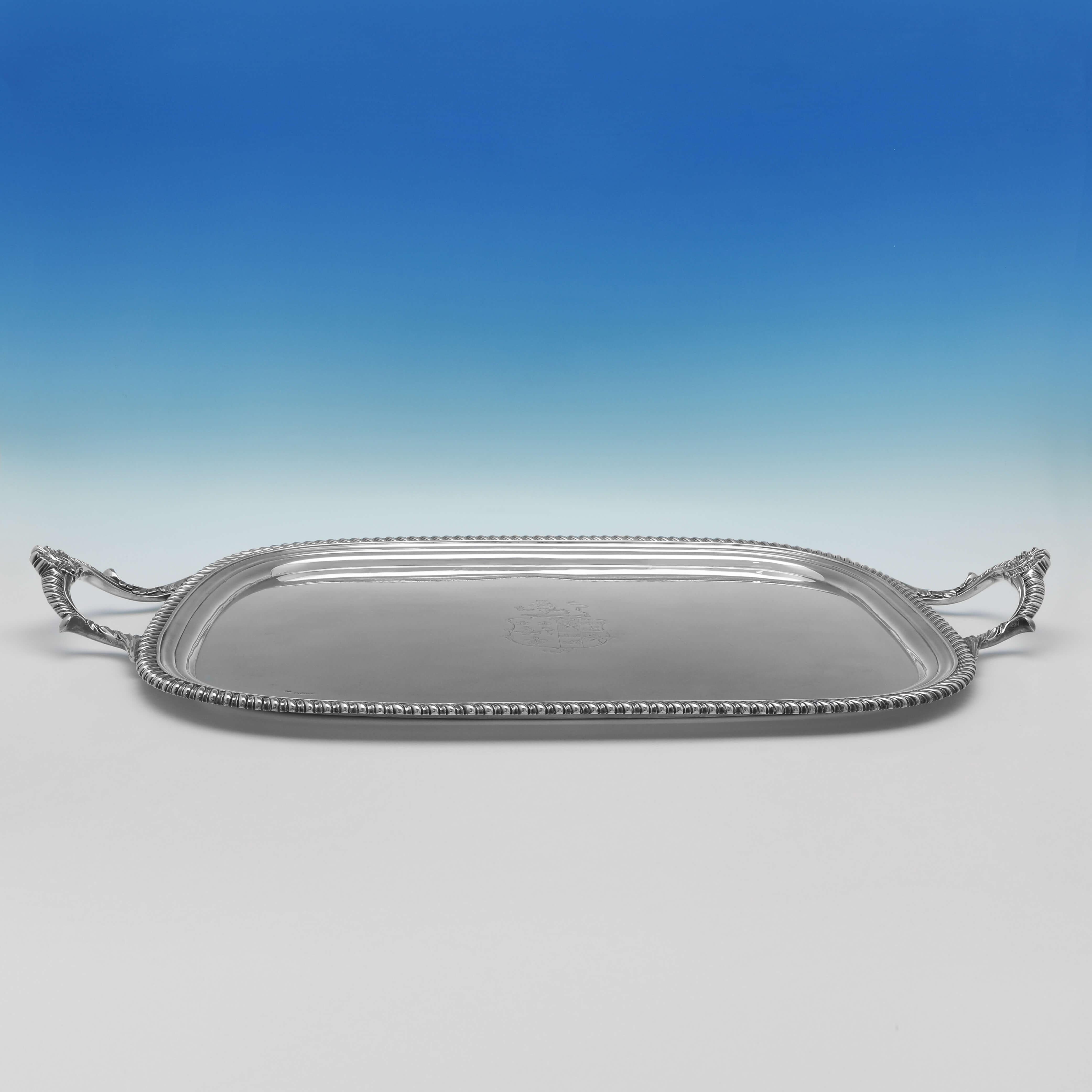 Hallmarked in London in 1814 by William Bennett, this large, Regency Period, Antique Sterling Silver Tray, features a gadroon border, shell and gadroon detailed handles, and an engraved coat of arms to the centre. The tray measures 32