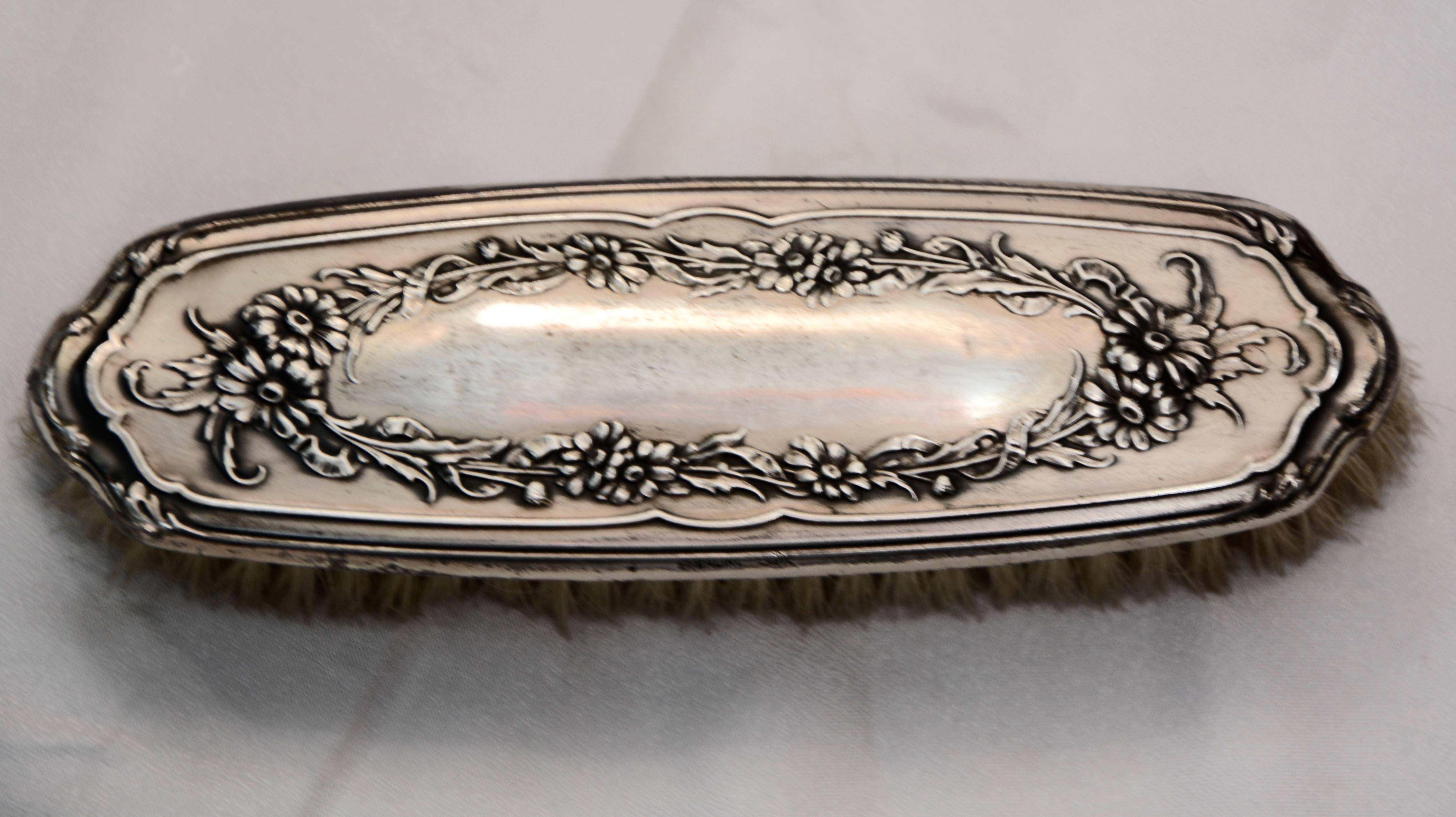 A lovely garland of flowers surrounded by a swirled border decorate the sterling silver of this Victorian clothes brush. It is marked on the side. Natural bristles will gently brush your clothing.