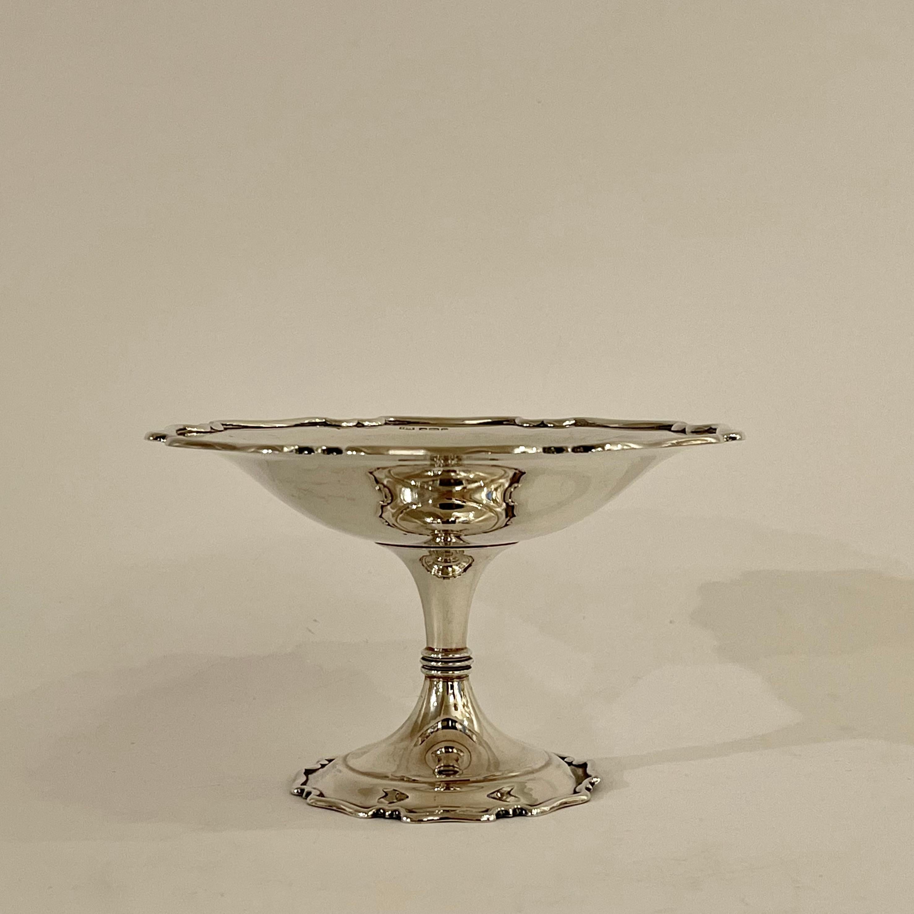 This small solid sterling silver late Edwardian Tazza dish is tastefully edged at the rim of the bowl and the base with a raised lip that ribbons between indented cusped arches. The pedestal steps once and funnels to a thin reeded band at its