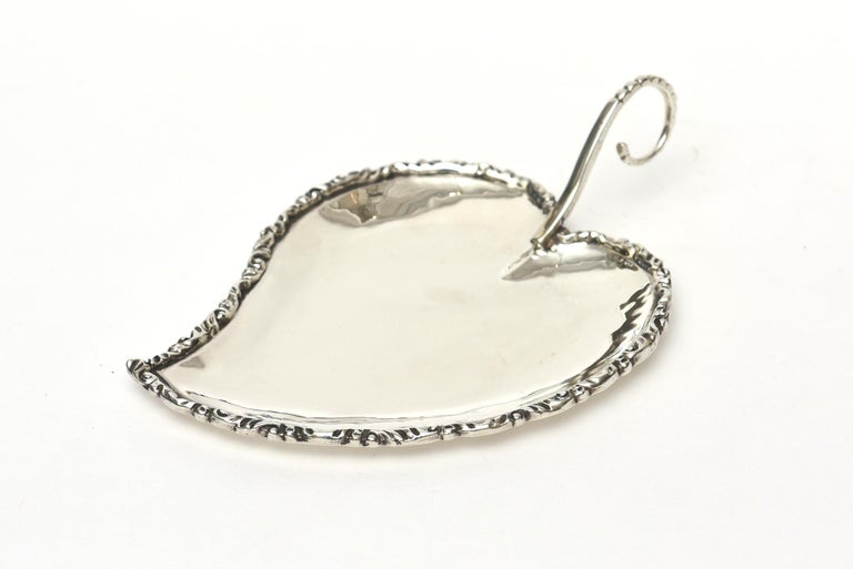 This lovely sterling silver hallmarked heart shaped leaf bowl and or dish has raised dimensional perimeter edges. It is marked on the Bottom as such: 925 with a script block R and sterling silver. The handle has a semi circle. This can be used for a