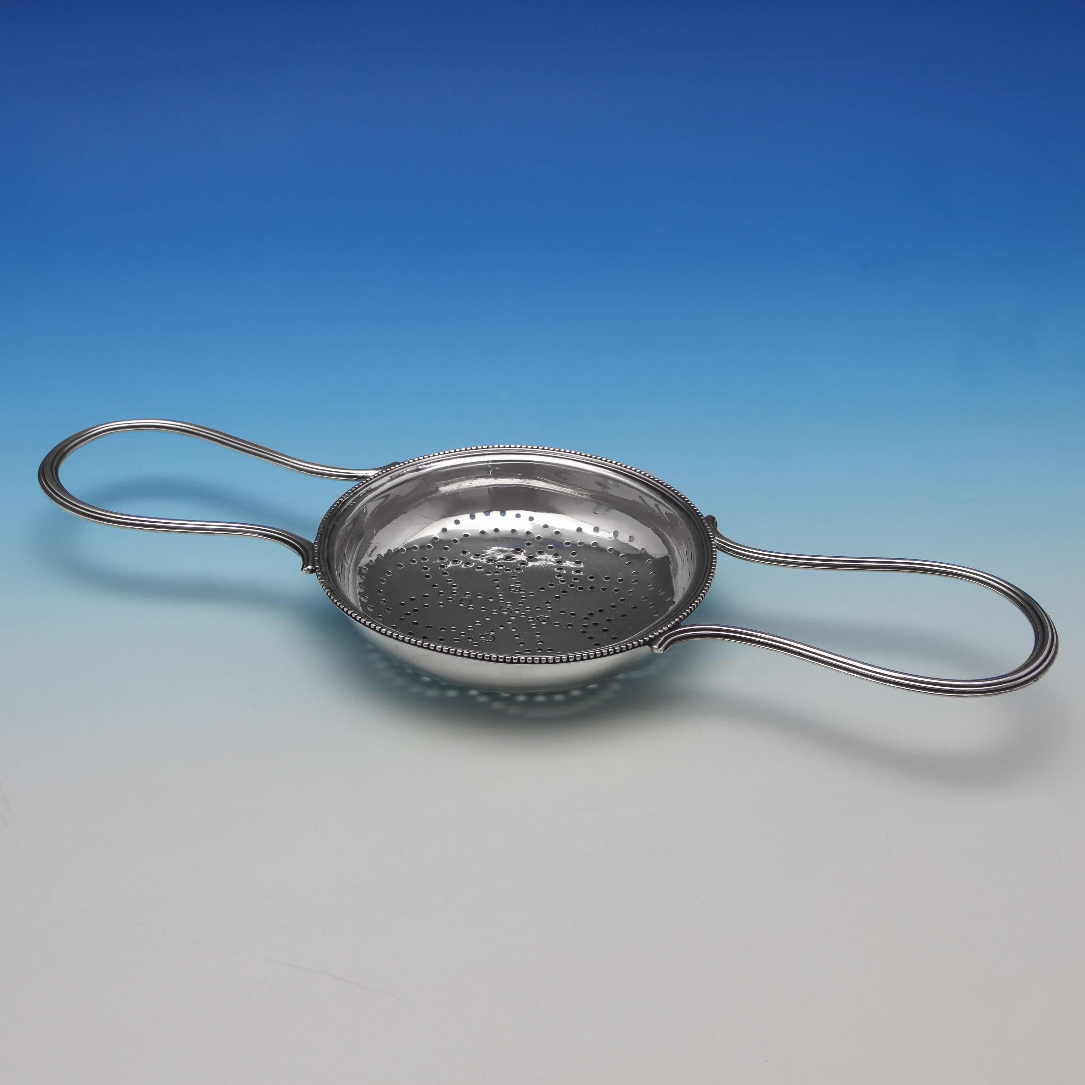 Hallmarked in London in 1786, this lovely antique, George III, sterling silver lemon strainer features daisy pattern piercing, a beaded border, and reeded loop handles. It measures 11