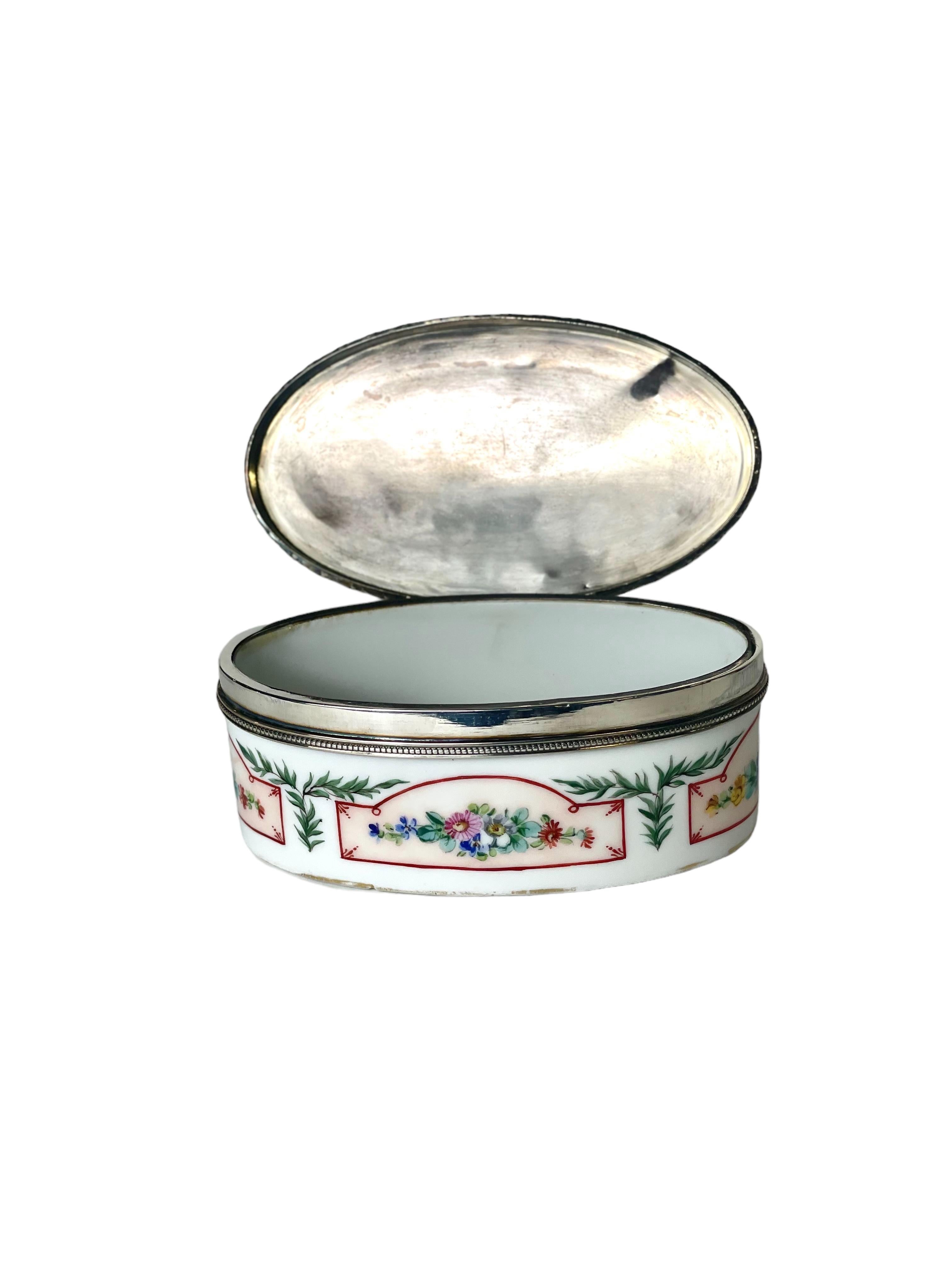 Une charmante petite boîte en porcelaine à couvercle en argent sterling, probablement utilisée pour le tabac à priser, ou pour des bibelots en général. Le plateau en argent est décoré dans le style Louis XVI et porte le poinçon d'argent de la tête