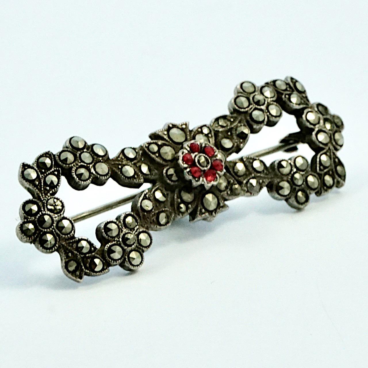 Beautiful sterling silver bow brooch with a flower and leaf design, and set with marcasites and a red paste stone centre flower. Measuring length 5.15 cm / 2 inches by width 1.85 cm / 1.73 inch. It is in very good condition, there is some wear to a