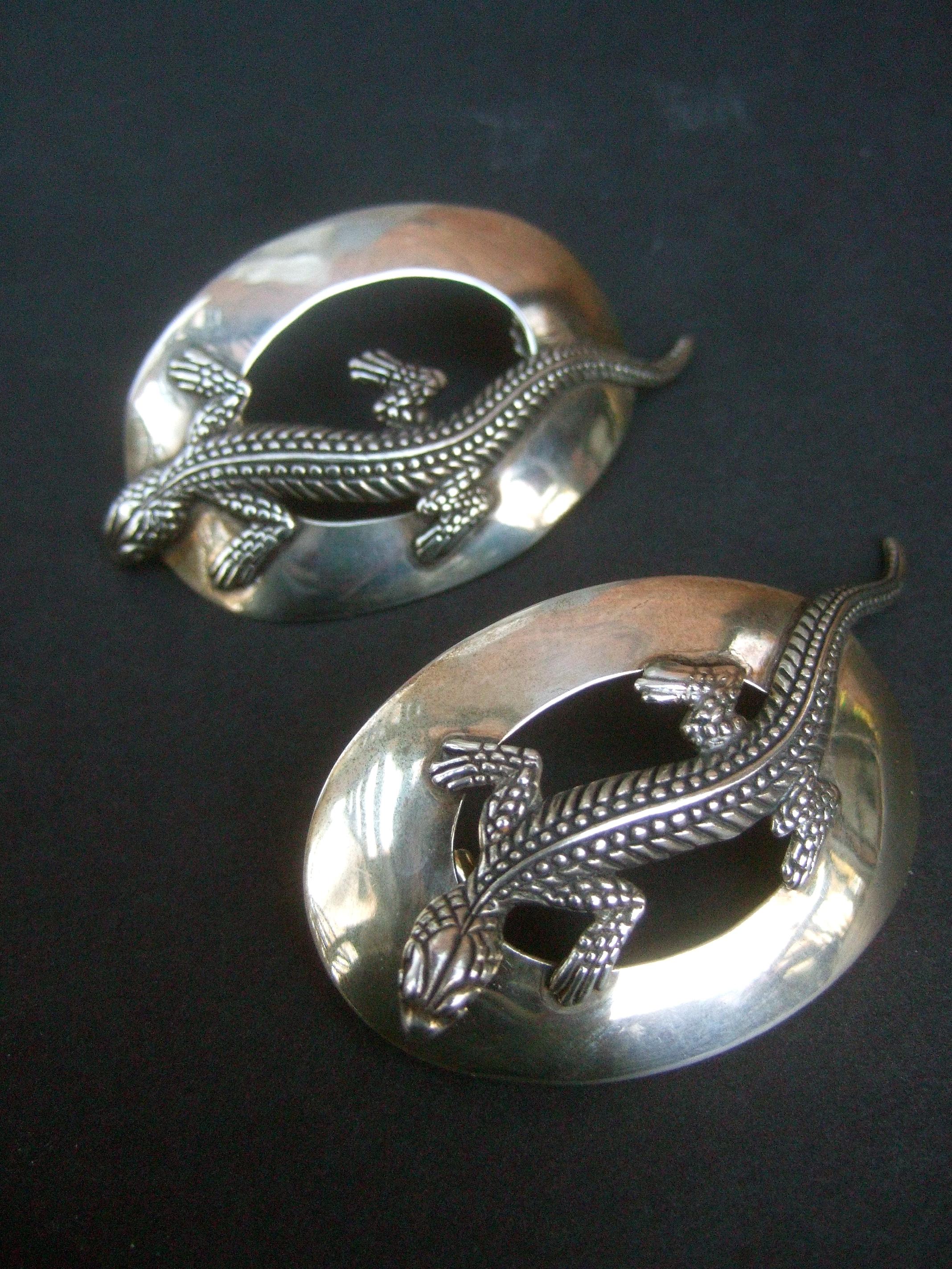 Sterling silver massive figural lizard artisan pierced earrings c 1990
The large scale artisan earrings are designed with a sinuous lizard figure; embellished with impressed and etched detail emulating scales

In contrast, the sterling oval-shaped