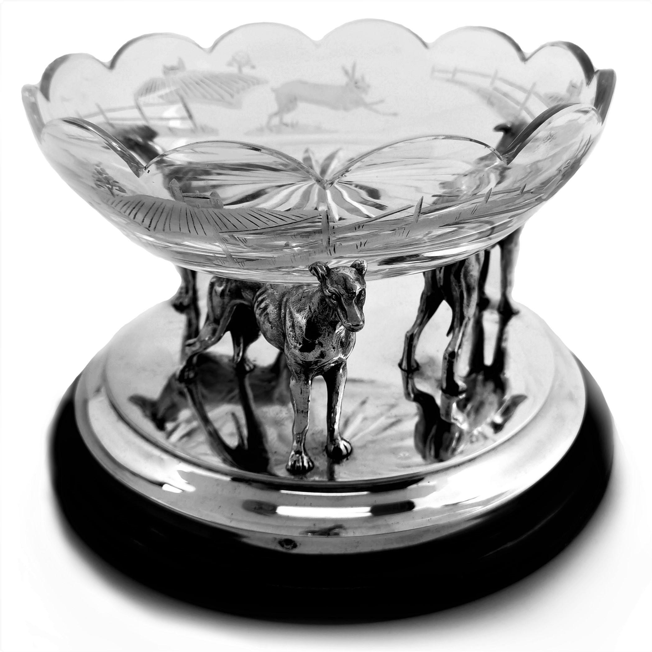 A gorgeous vintage solid Silver model of three Greyhounds standing on a circular silver base on a black circular plinth with an elegant clear class etched bowl resting on the greyhounds. Each Greyhound Faces outward in different directions making a