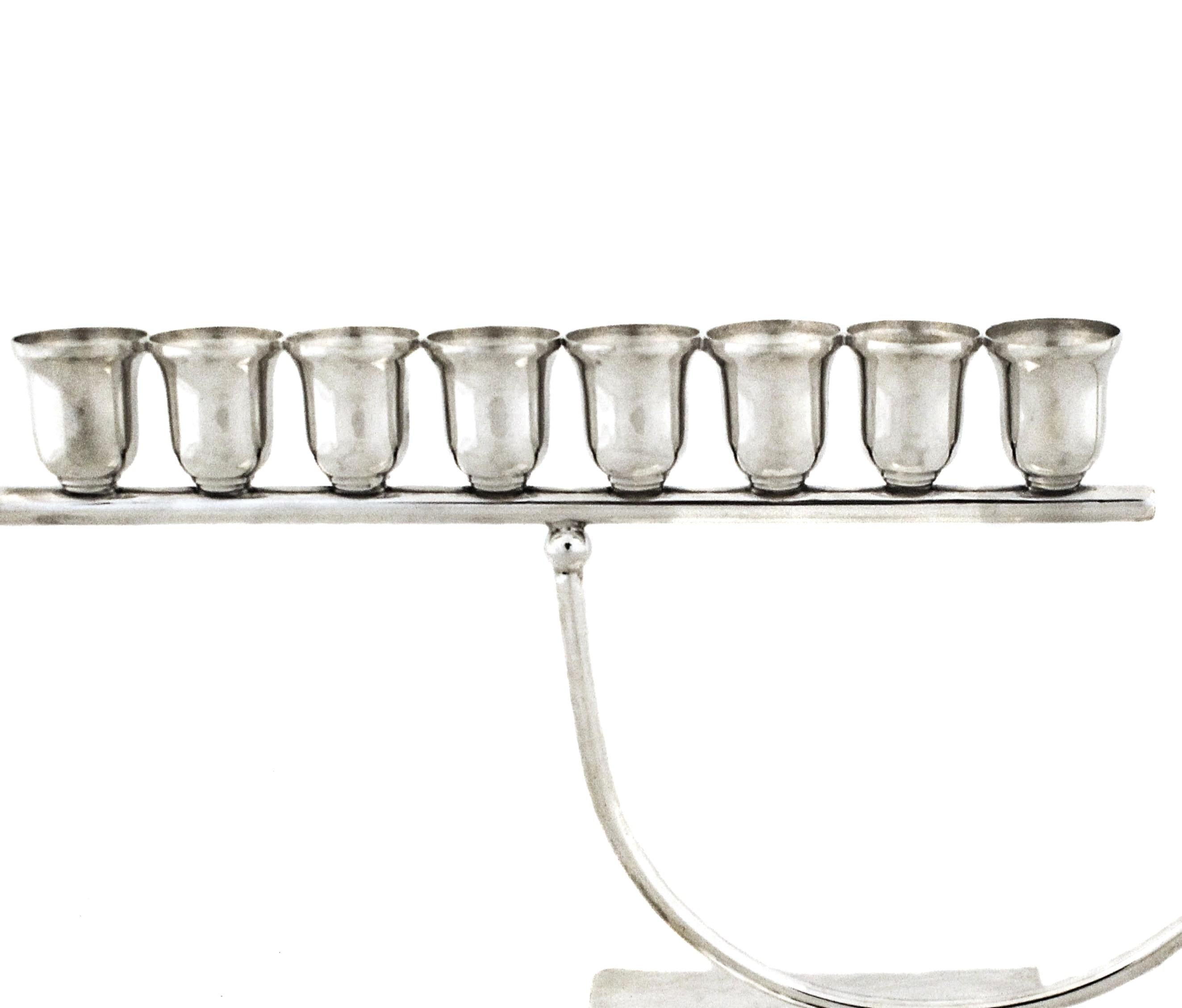 Orgullosos de ofrecer esta moderna menorá de plata de ley para celebrar una tradición milenaria.  Un tubo singular conecta las ocho luces con el 