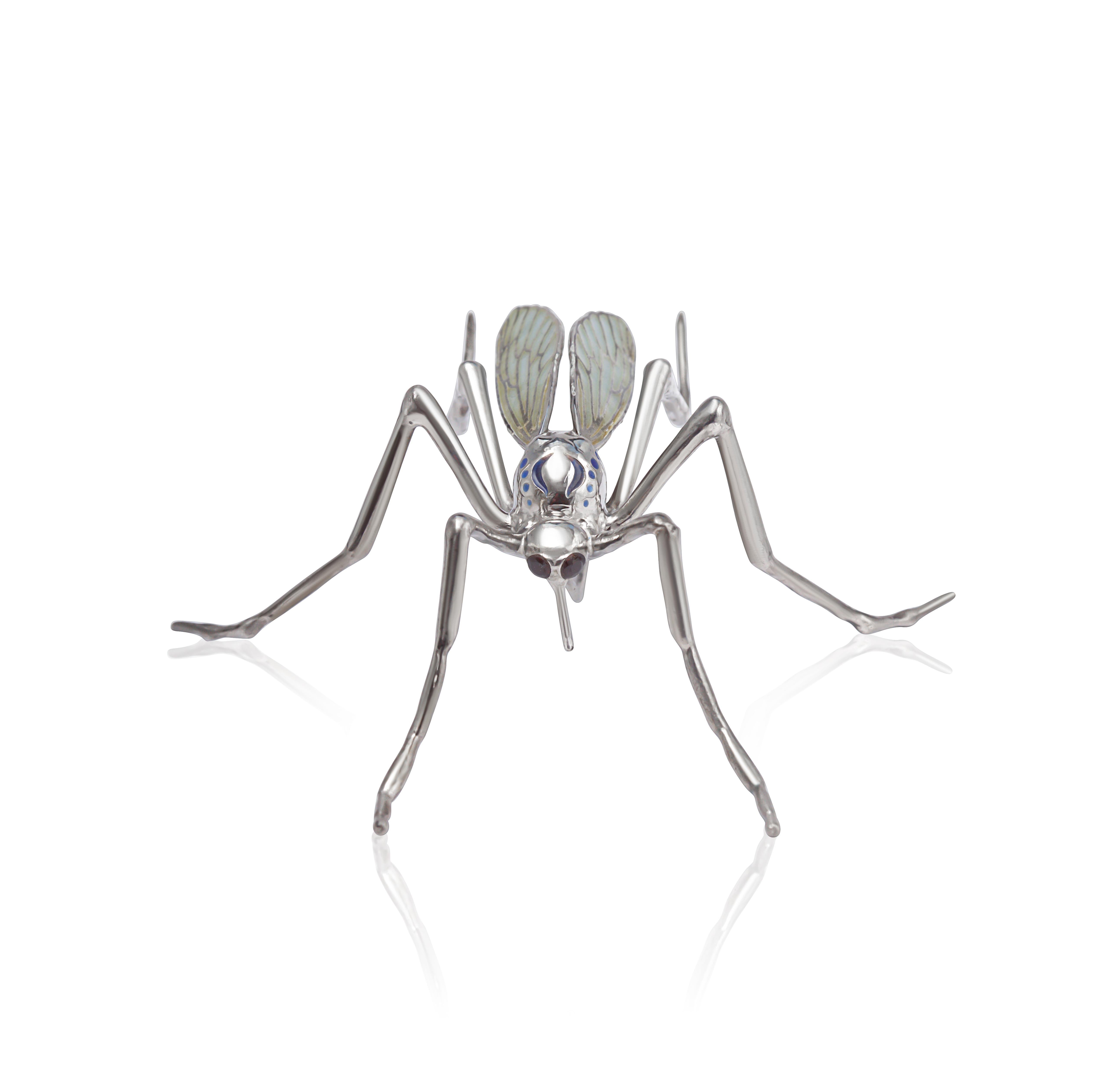 Cette broche unique est fabriquée à la main en argent sterling oxydé, conçue sous la forme d'un moustique méticuleusement détaillé. Le corps et les jambes sont sculptés avec précision, tandis que les yeux sont sertis de grenats d'un rouge profond