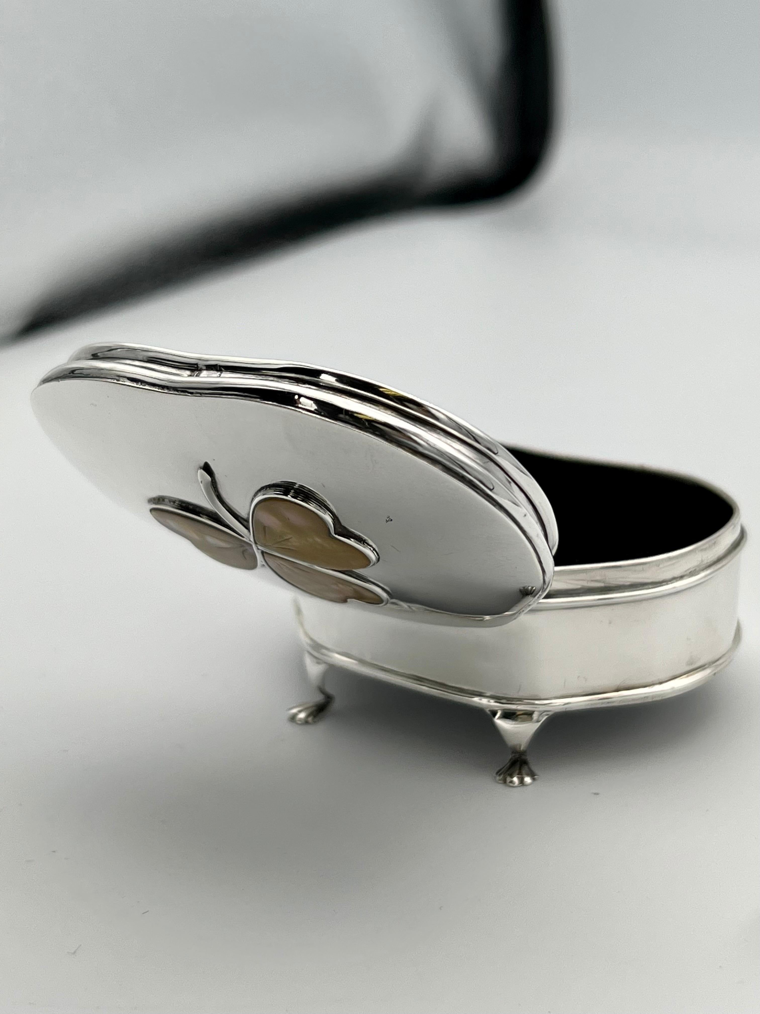Lovely and unique hinged jewelry box. Graceful bowed shape. On four legs with paw feet. On top is an applied clover or trefoil, inlaid with mother-of-pearl . Very solid gauge silver. The inside top and bottom have a soft black velvet lining. 3 1/4