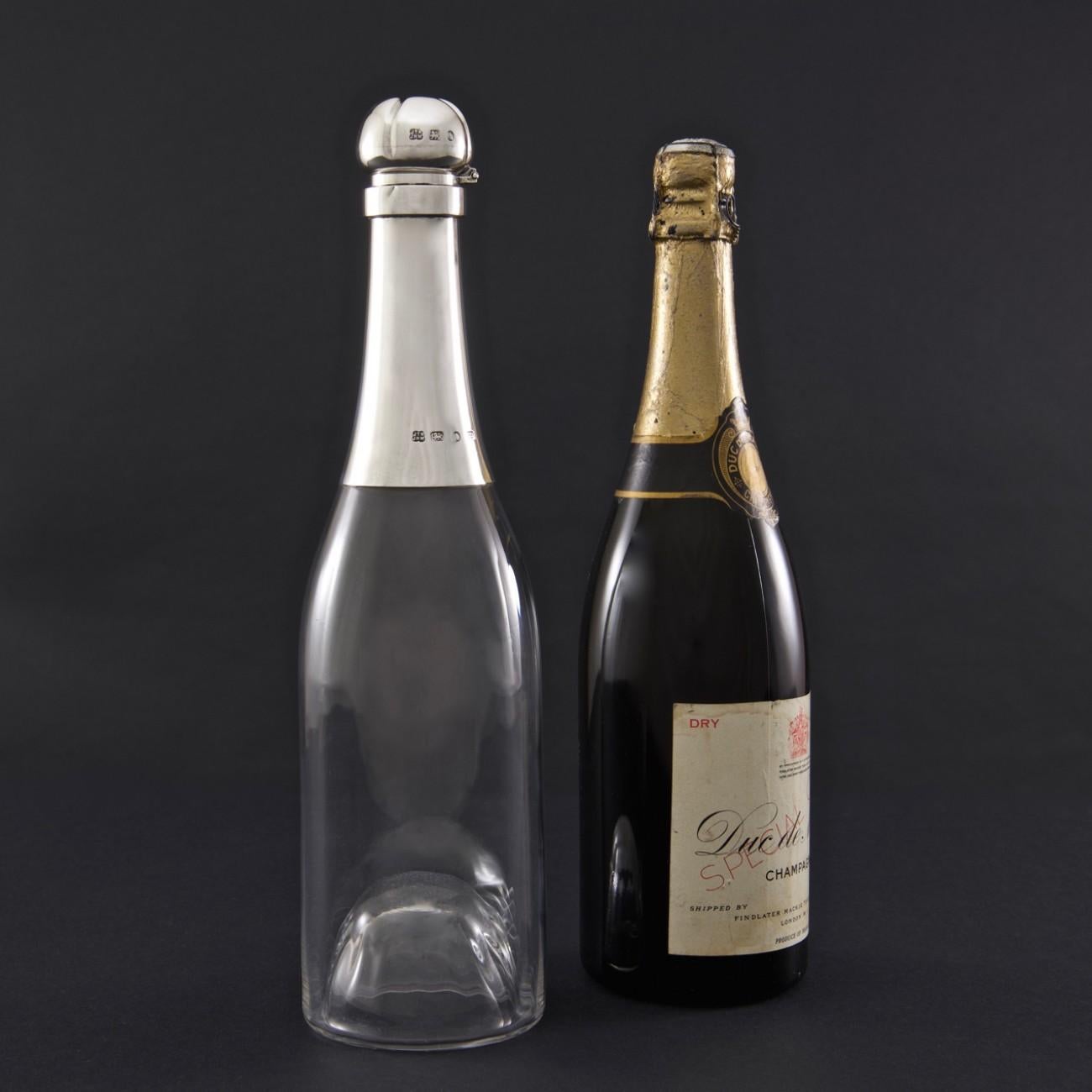 Wonderful decanter with a bottle capacity, modelled as a Champagne bottle. The glass body is fluted, but in a truly elegant fashion, on the inside only; so that the outside surface of the decanter remains smooth. The silver neck and hinged stopper