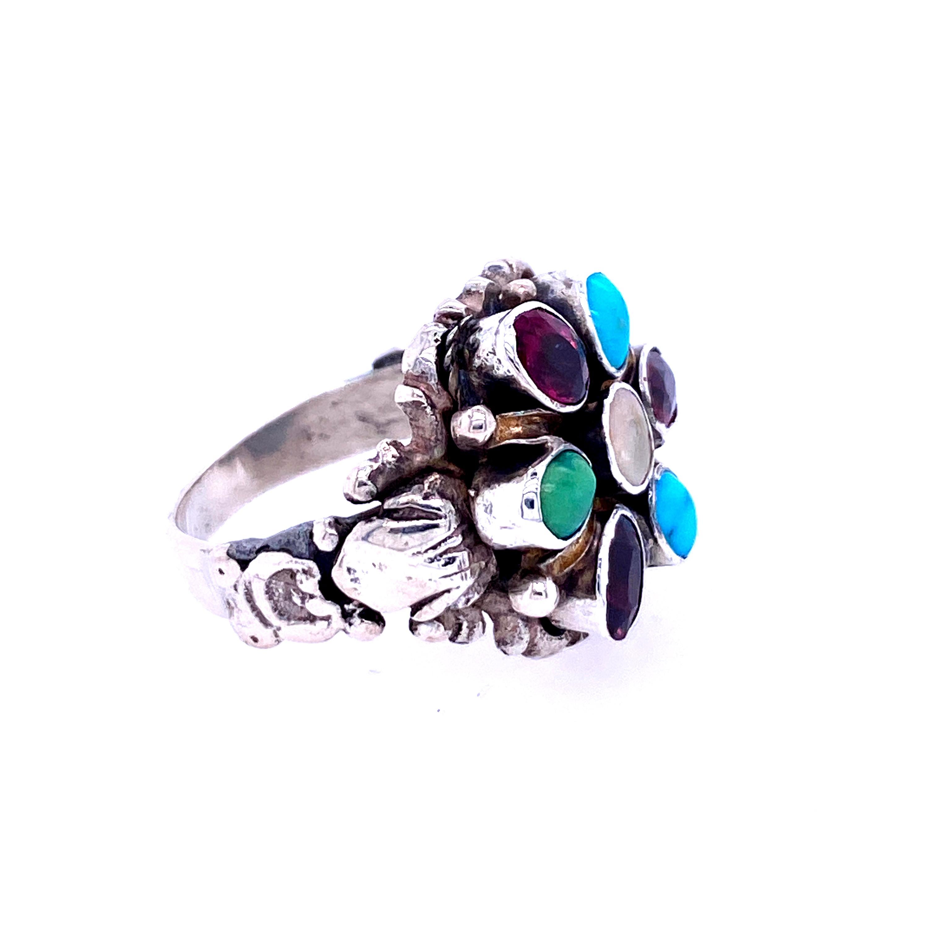 One sterling silver cluster ring set with one center 5mm round mother of pearl, surrounded by three oval garnets measuring 5x3mm  and three oval turquoise stones measuring 5x3mm .  The shank measures 6mm near the top of the ring and tapers to 3mm at
