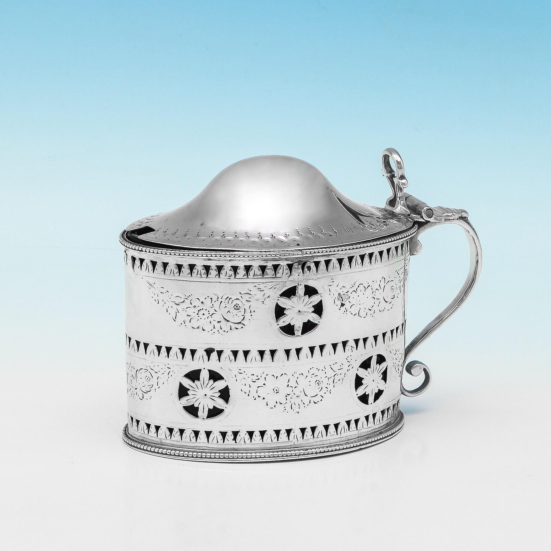 Hallmarked in London in 1787 by Hester Bateman, this handsome George III, antique, sterling silver mustard pot has floral engraving and pierced decoration, typical of Bateman's style. Featuring a domed, hinged lid and a blue glass liner, the mustard