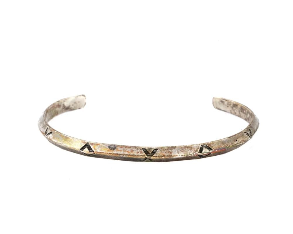 A Native American Navajo Sterling Silver bangle cuff. The thin bracelet has a raised edge in the middle and is decorated with a minimalist repeating pattern of small triangles. Circa: 1960s. Vintage and Modern Native American Ethnic Jewelry,