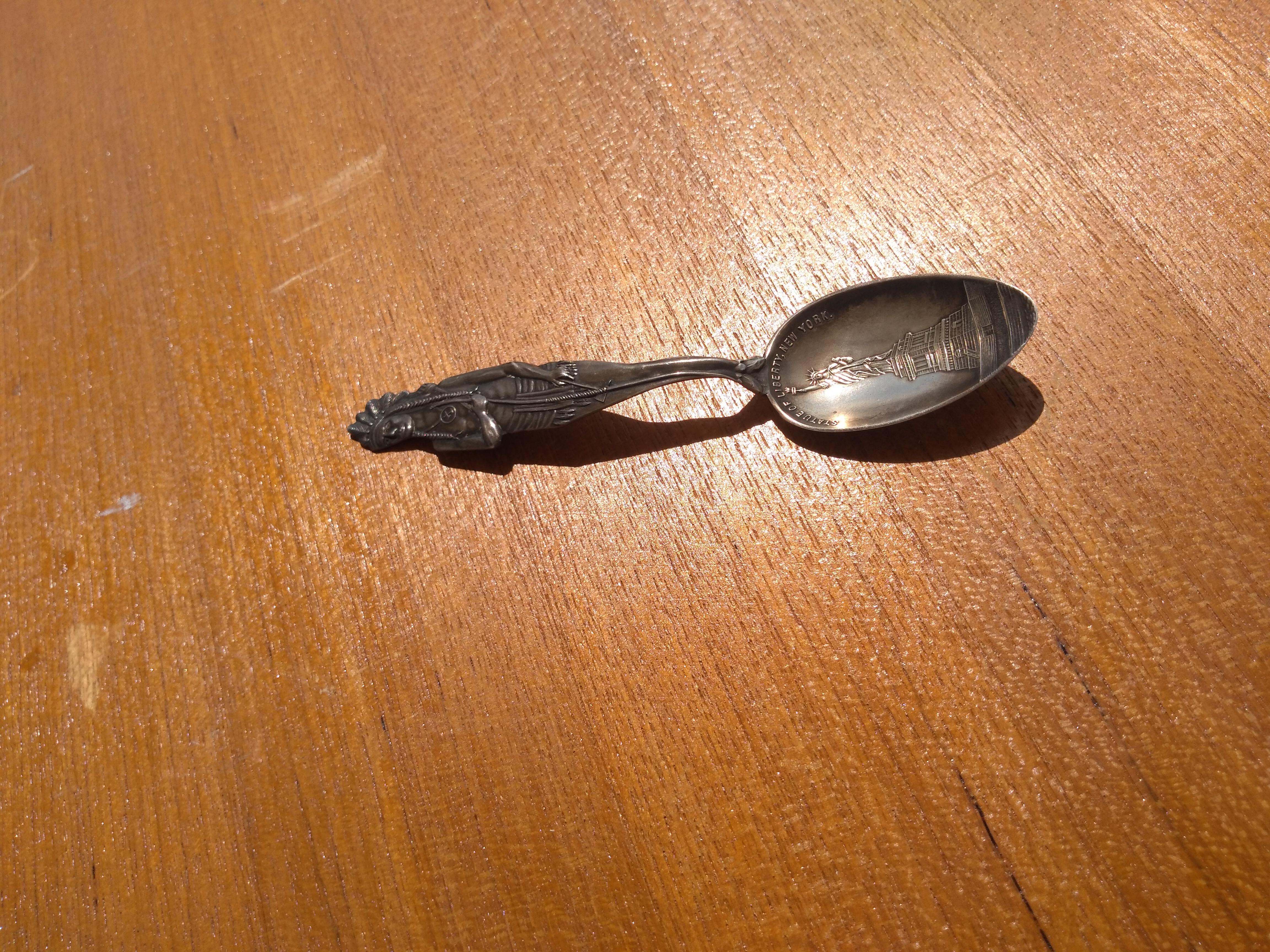 This spoon is made of sterling silver. It has a Native American figure cast on the handle. It's the complete figure being the front and back. The well of the spoon has the Statue of Liberty engraved in it. The spoon has a weathered patina.