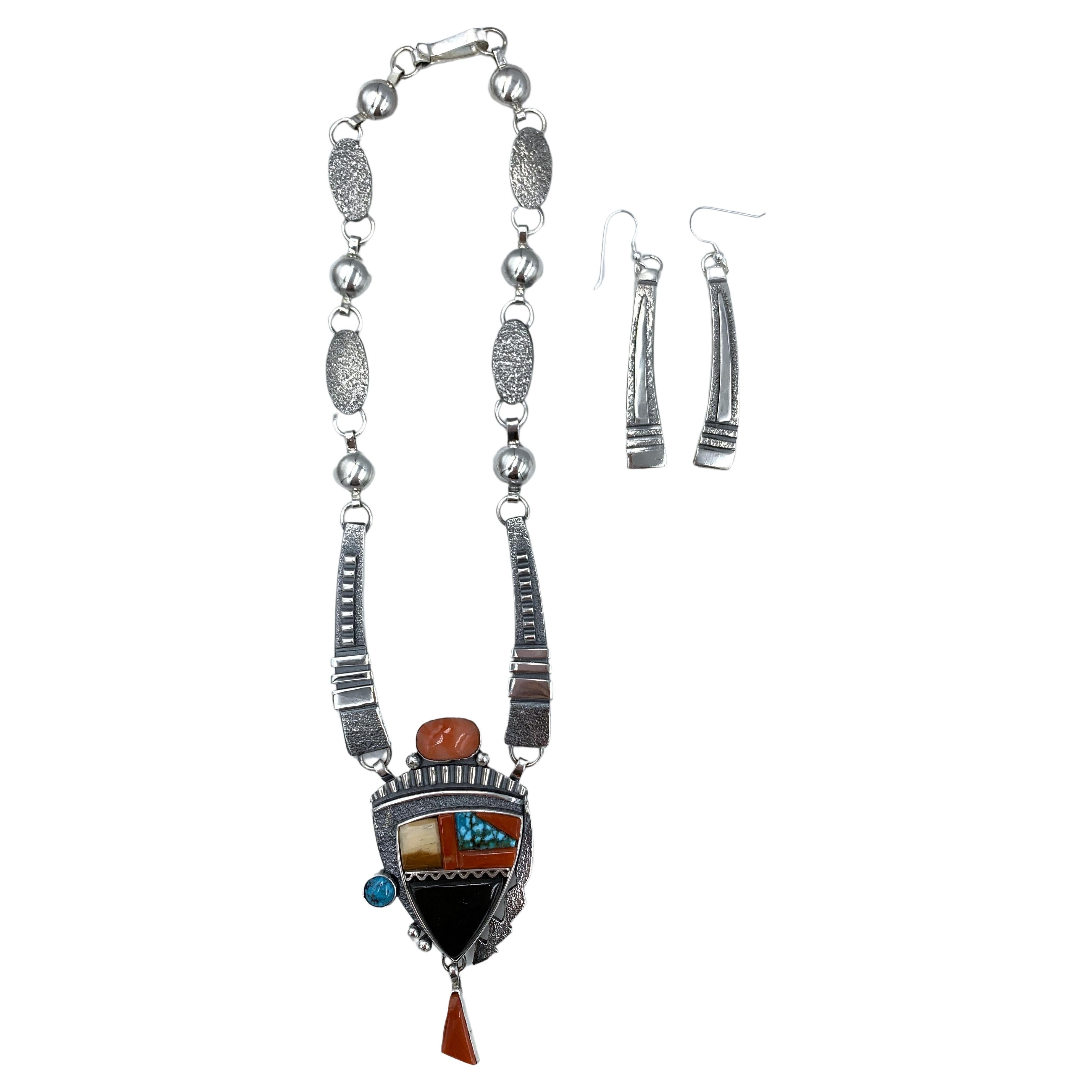 Sterling silver and inlay necklace and earrings set by Navajo silversmith Jack Tom. The pendant has turquoise, jet, jasper, coral, spiney oyster.

Tom's signature design is sleek and elegant with refined oxidized ridges against bright sterling