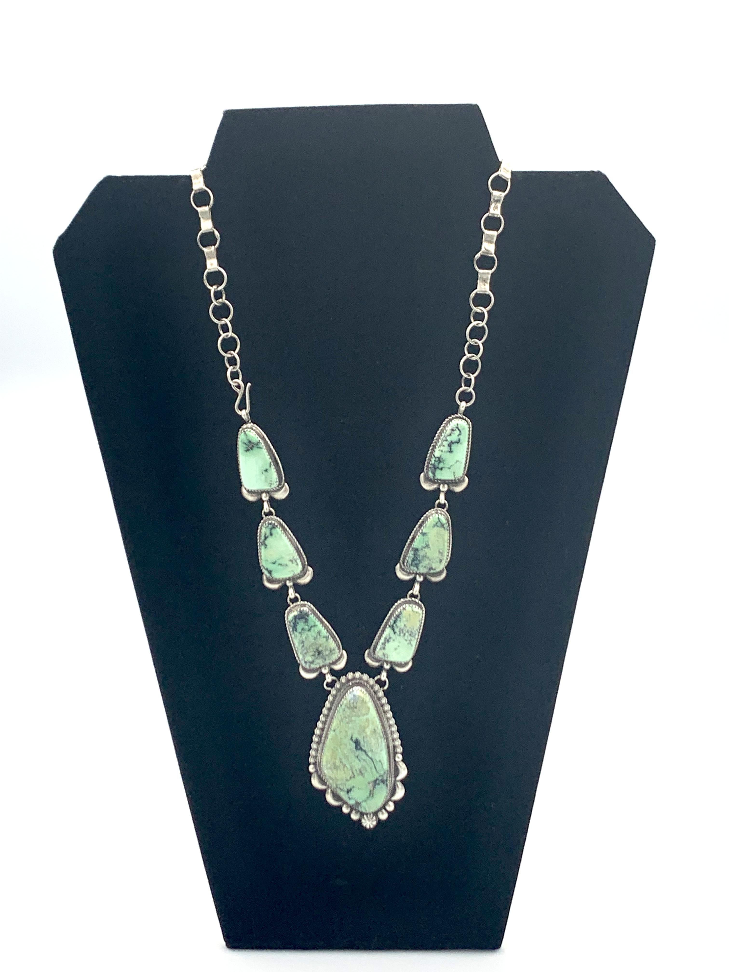 Questa straordinaria collana in argento sterling presenta sette pietre di turchese Dry Creek tagliate e lucidate a mano, di cui una elegantemente sospesa come ciondolo. La collana è composta da una catena d'argento con maglie ovali e rettangolari