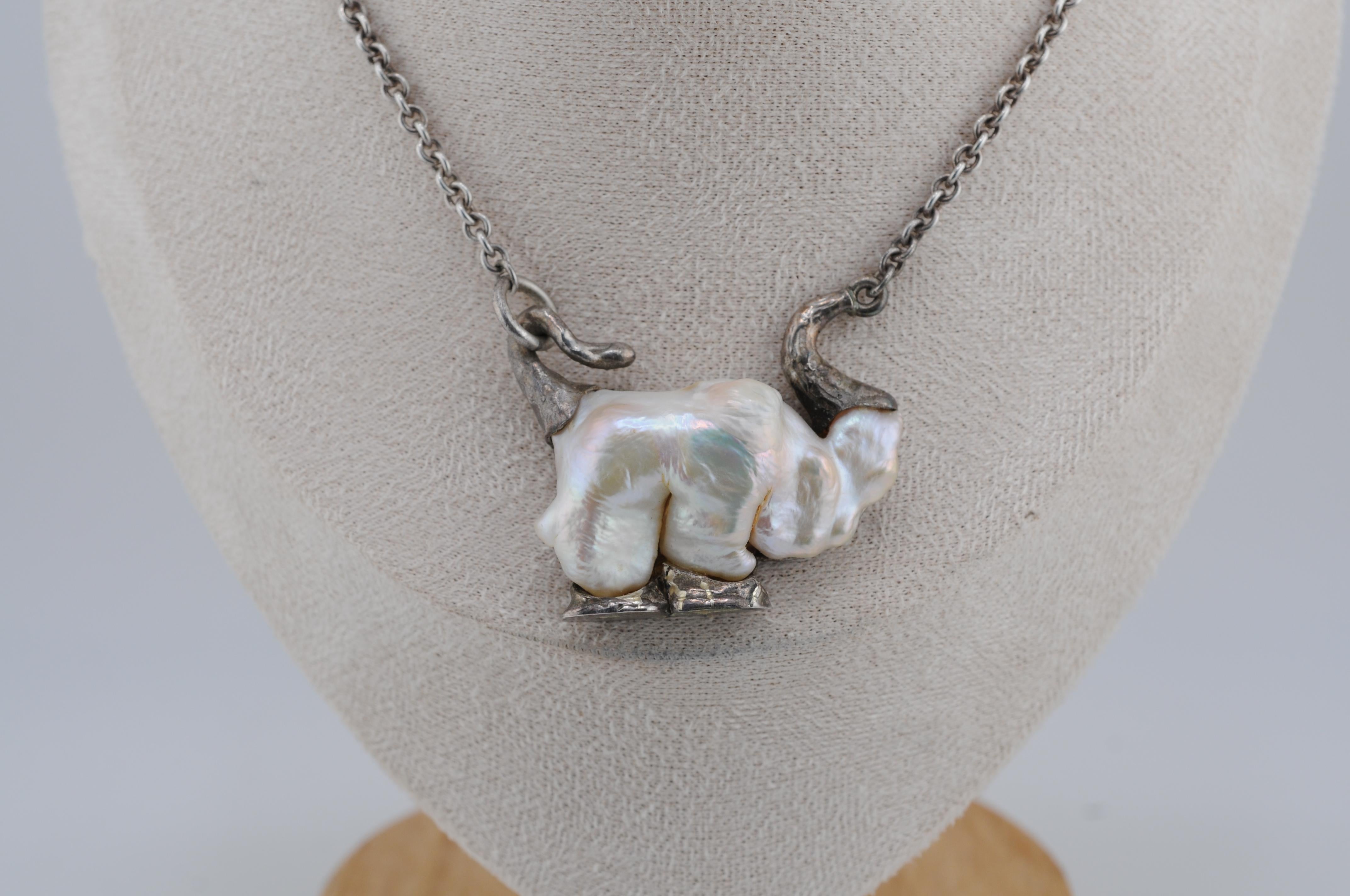 Collana insolita e organica con una grande perla Keshi dalla forma naturale che ricorda la silhouette di un elefante. Incastonato in argento sterling con sottili accenti metallici, questo pezzo celebra l'arte e l'individualità della natura. Un'idea