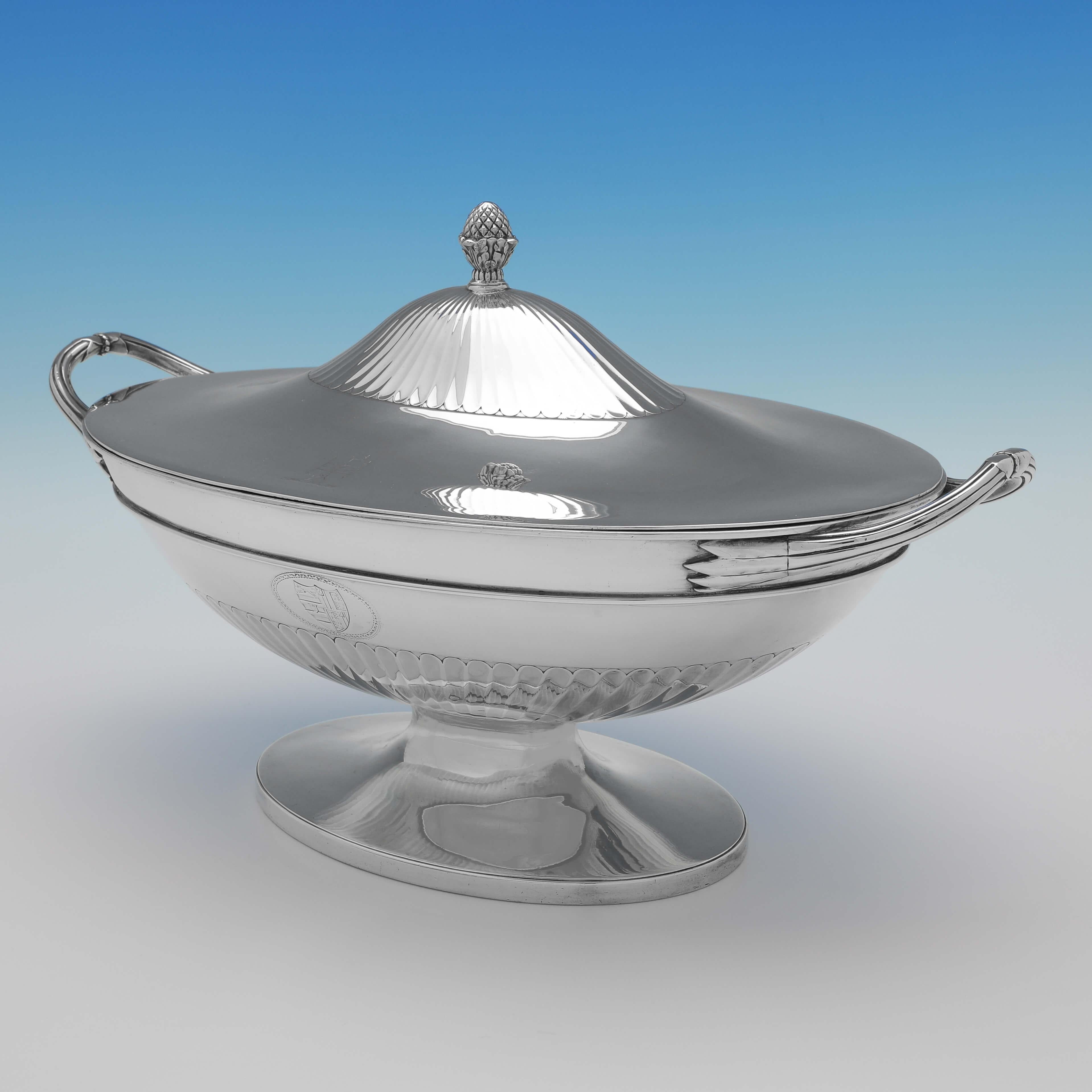 Hallmarked in London in 1784 by John Wakelin & William Taylor, this handsome, George III, Antique Sterling Silver Soup Tureen, is Neoclassical in style, featuring sunken half fluting to the body and lid, reed borders, an engraved coat of arms and an