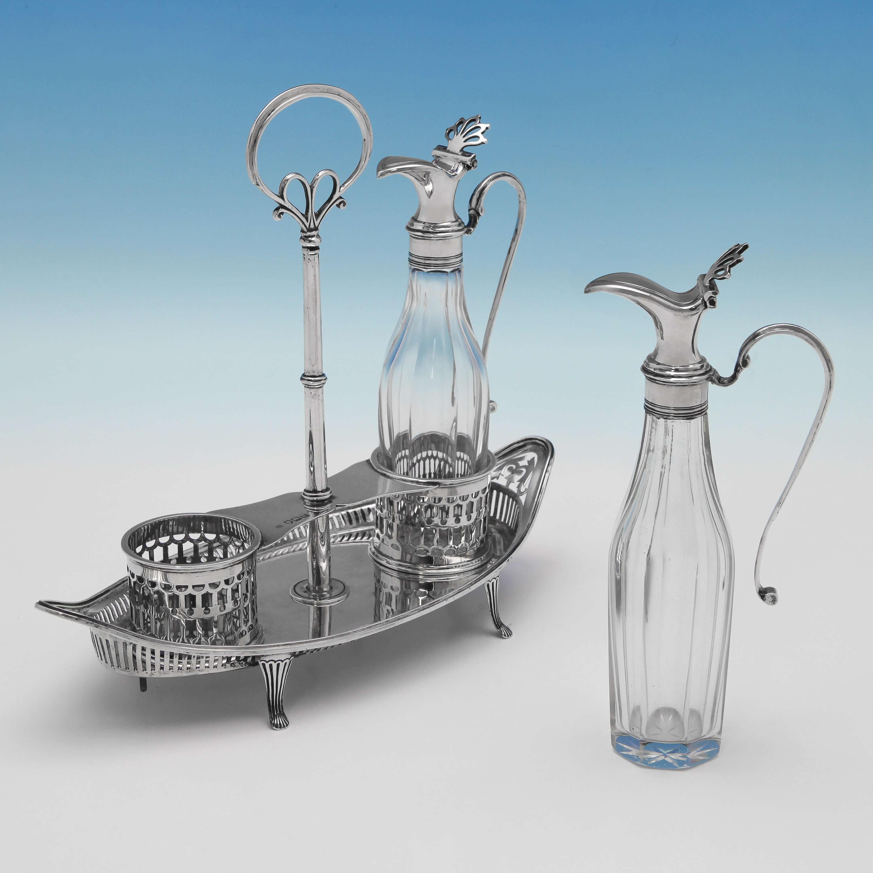 Hallmarked in London in 1899 by Thomas Bradbury & Sons, this stylish Antique, late Victorian, Sterling Silver Oil And Vinegar Set is in the George III style. The two panelled glass bottles with silver mounts and handles sit in a slat pierced oval