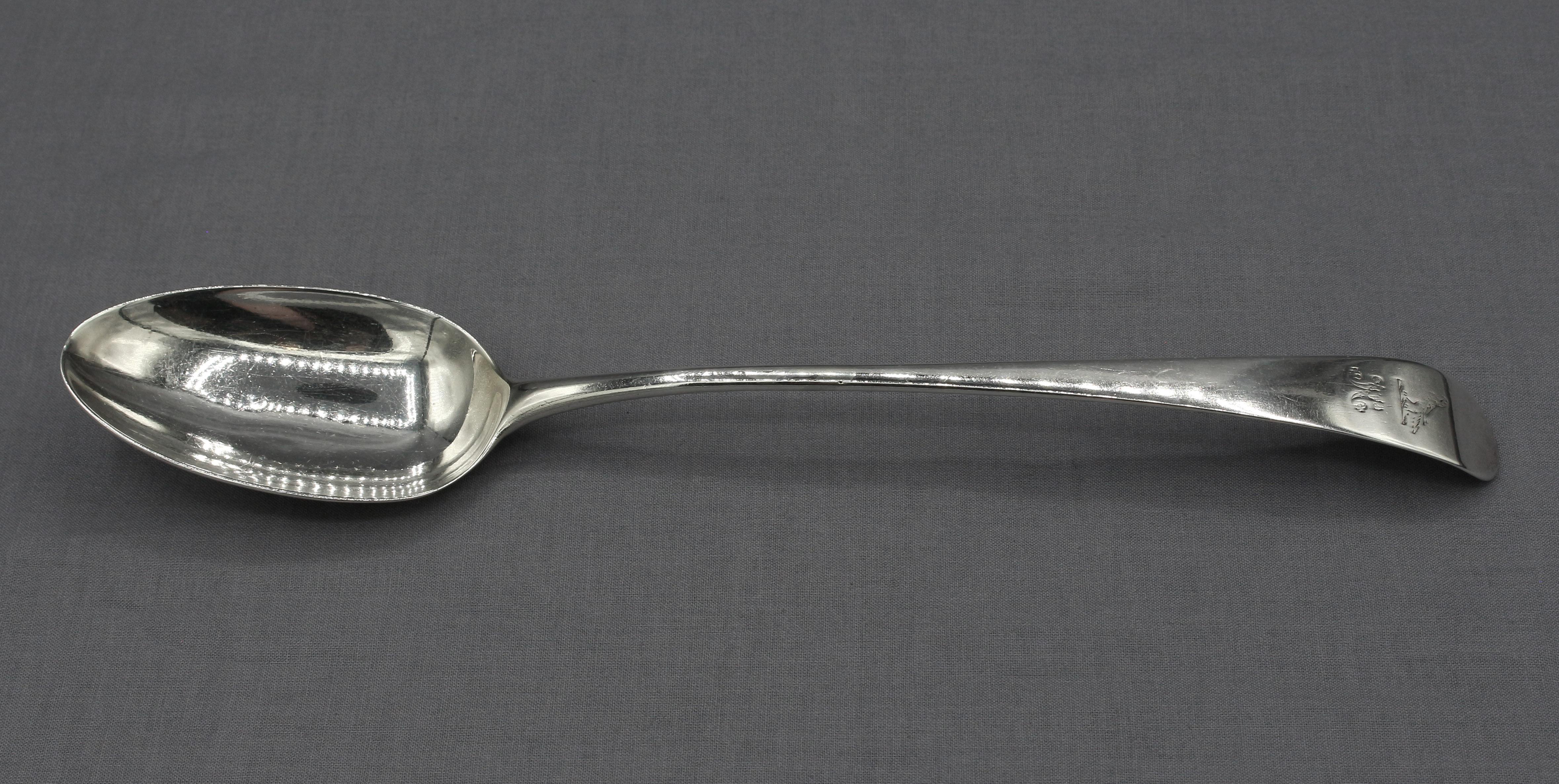 Sterling silver Old English basting spoon by Hester Bateman, 1785, London. Perhaps the most famous female silversmith for collectors. Family Crest of a hawk over a monogram (indistinct from wear). Very nice condition with wear on monogram & crest.