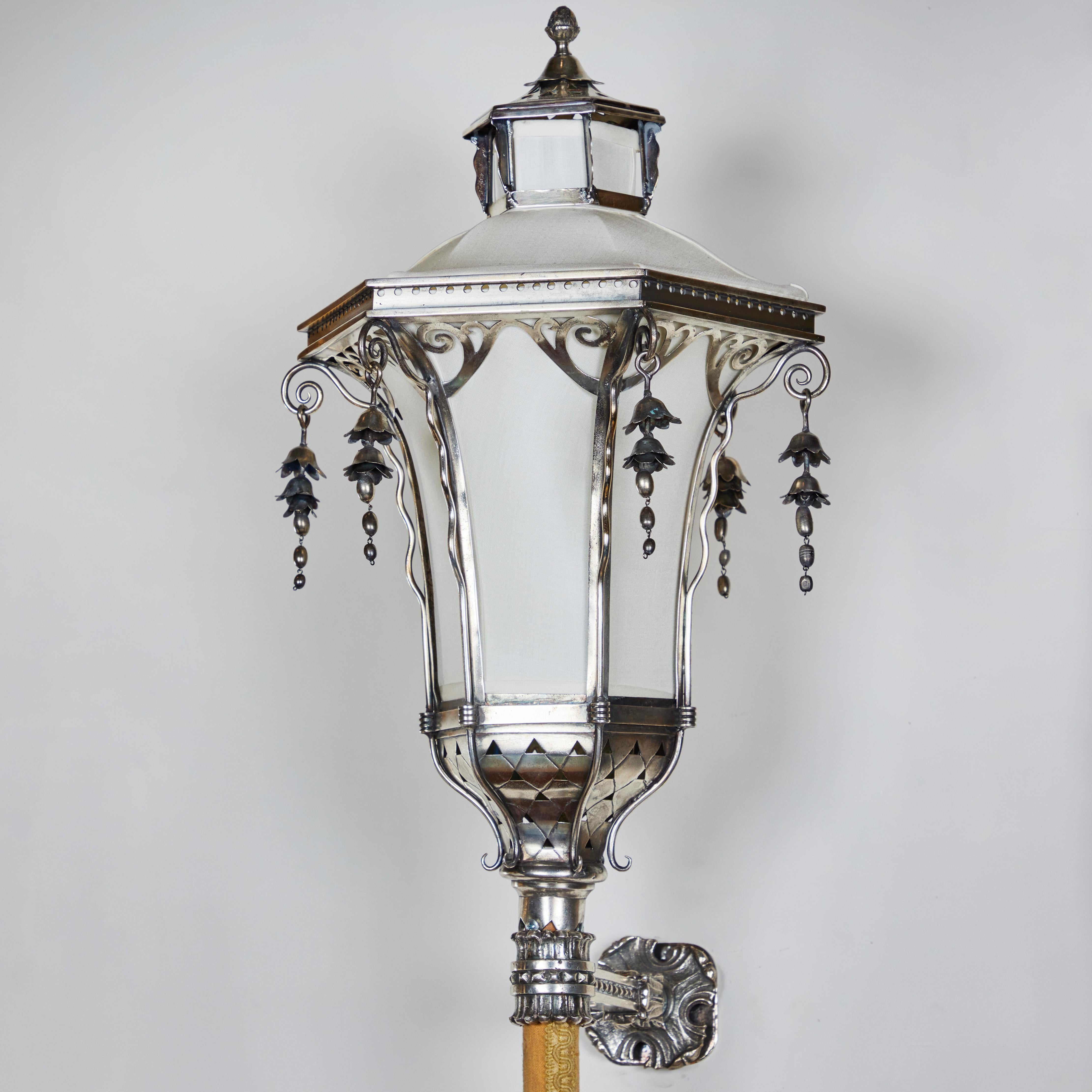 Sterling silver pagoda shaped wall sconce with bracket and new linen shade.  Pole covered in brocade fabric.  Metal cap at end of pole.  Top portion of shade lifts off to change light bulb. European wiring.  Liberty Period (1880-1920).