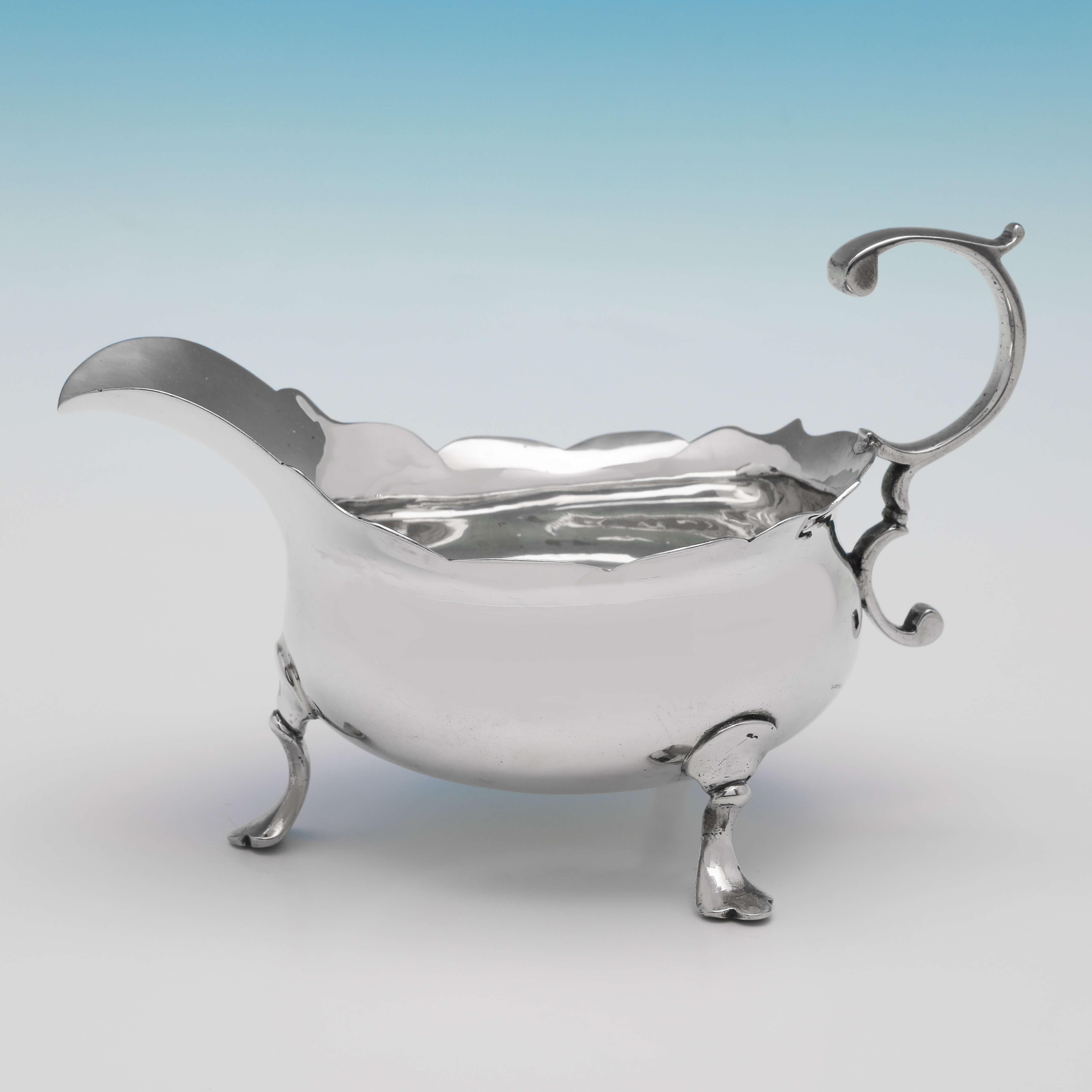 Hallmarked in London in 1751 by David Mowden, this handsome pair of George II, Antique Sterling Silver Sauce Boats, feature shaped edges, flying C-scroll handles, and stand on three feet. Each sauce boat measures 4