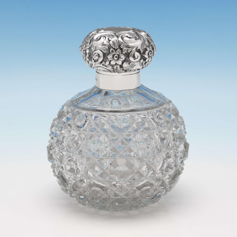 Hallmarked in Birmingham in 1898 by Synyer & Beddoes, this attractive pair of Victorian, Antique Sterling Silver Scent Bottles, feature hobnail cut glass bodies, and ornate lids with floral chasing. Each scent bottle measures 5.5