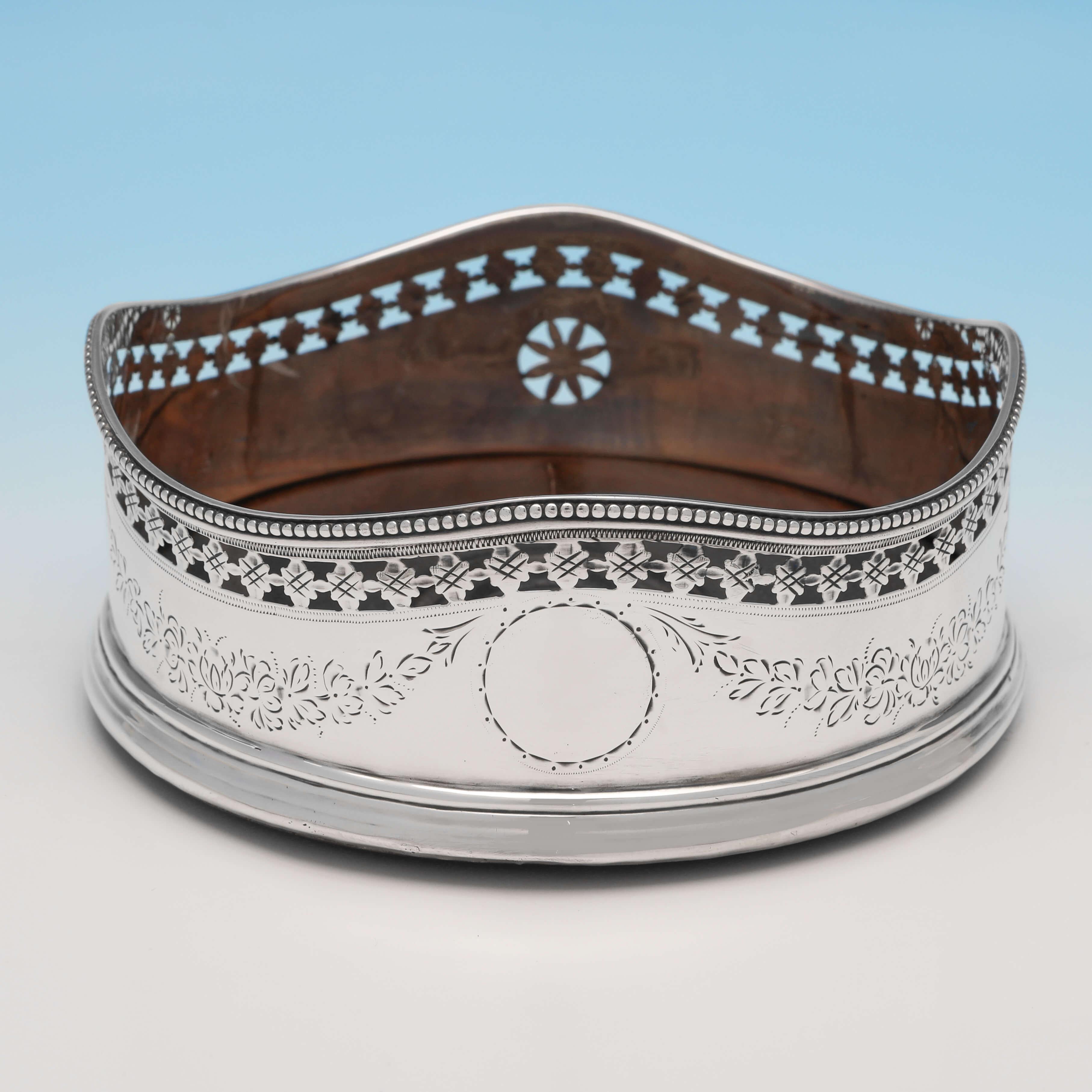 Hallmarked in London in 1787 by Hester Bateman, this very attractive pair of George III, antique sterling silver wine coasters, feature engraved and pierced decoration to the bodies, and shaped rims with bead borders. Each wine coaster measures