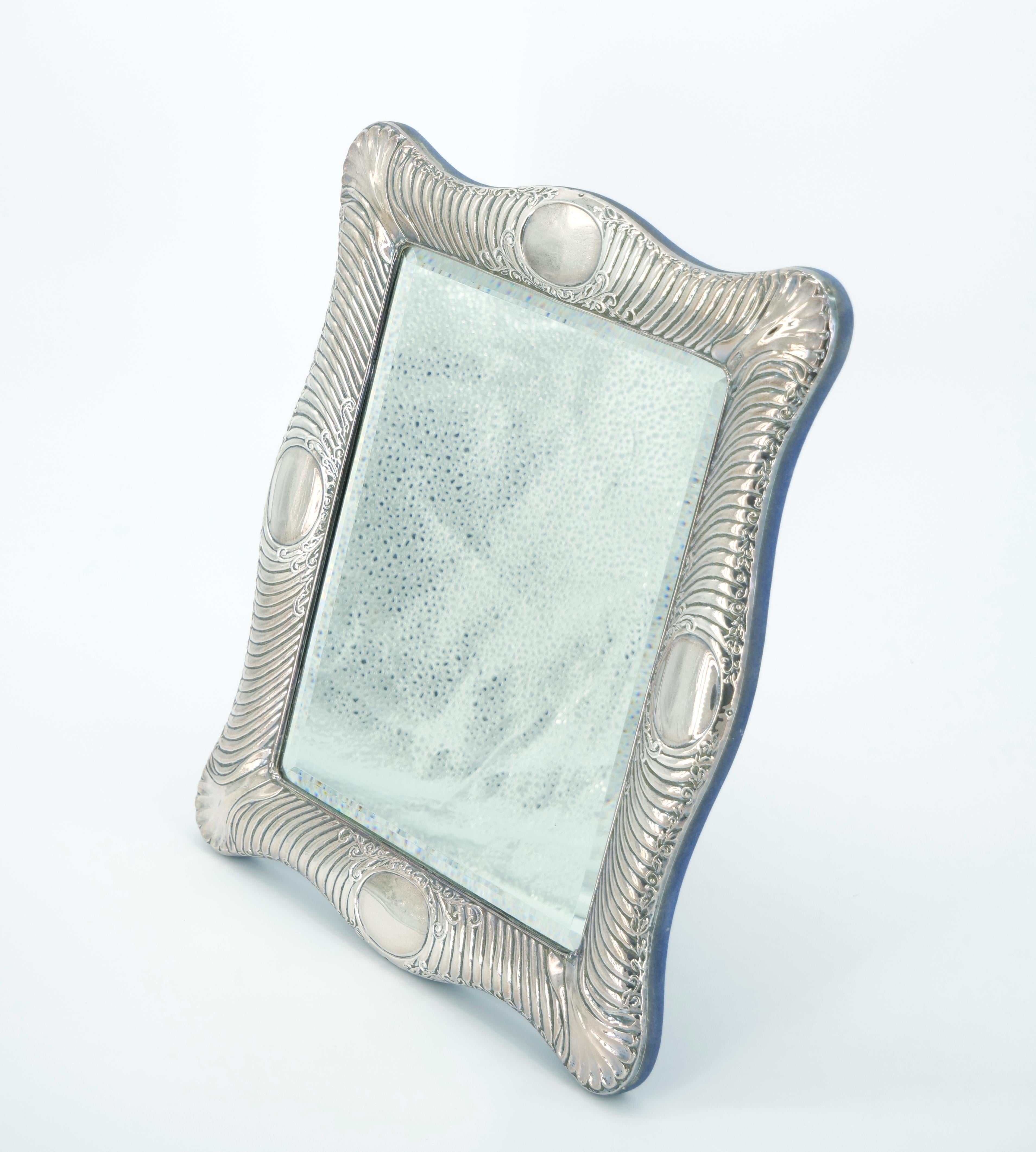 Enhance your vanity with this exquisite English Sterling Silver Framed Rectangle Table Mirror—a vintage masterpiece of refined craftsmanship. The thick sterling silver frame is adorned with intricate engraved details, featuring a thin wreath garland