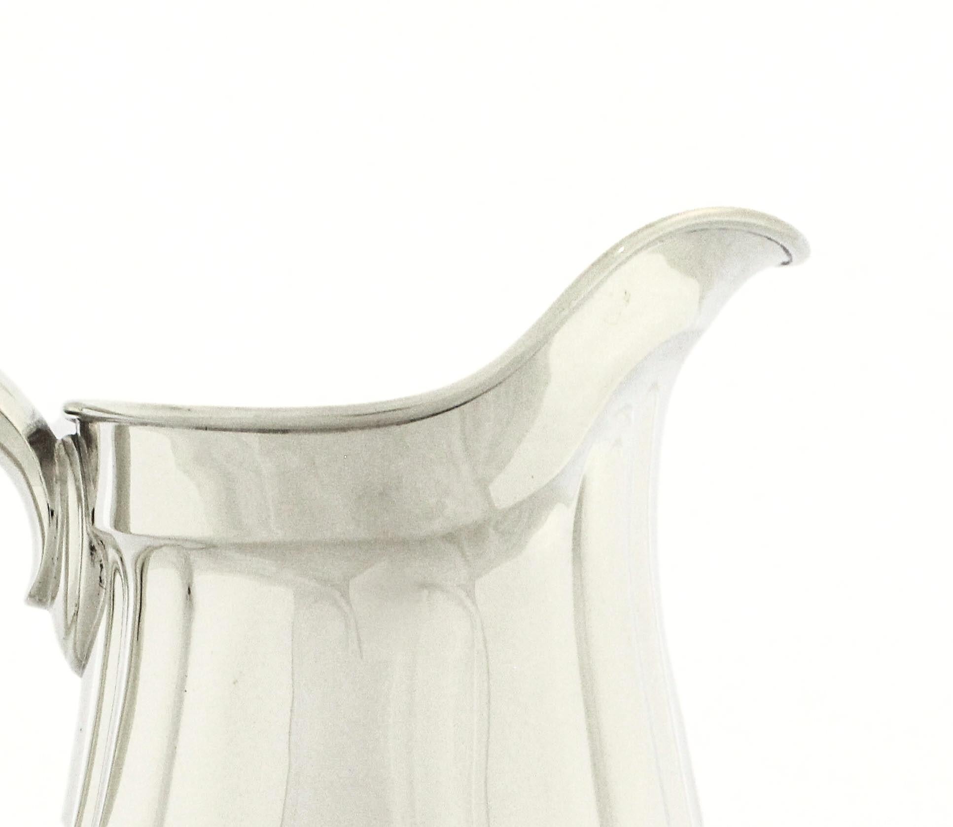 A classic and elegant sterling silver water pitcher by Reed & Barton, of graceful baluster form with a scrolling handle, flared spout, and gently lobed body rising from a circular, stepped foot. The pitcher’s surface is finely hand-polished to a