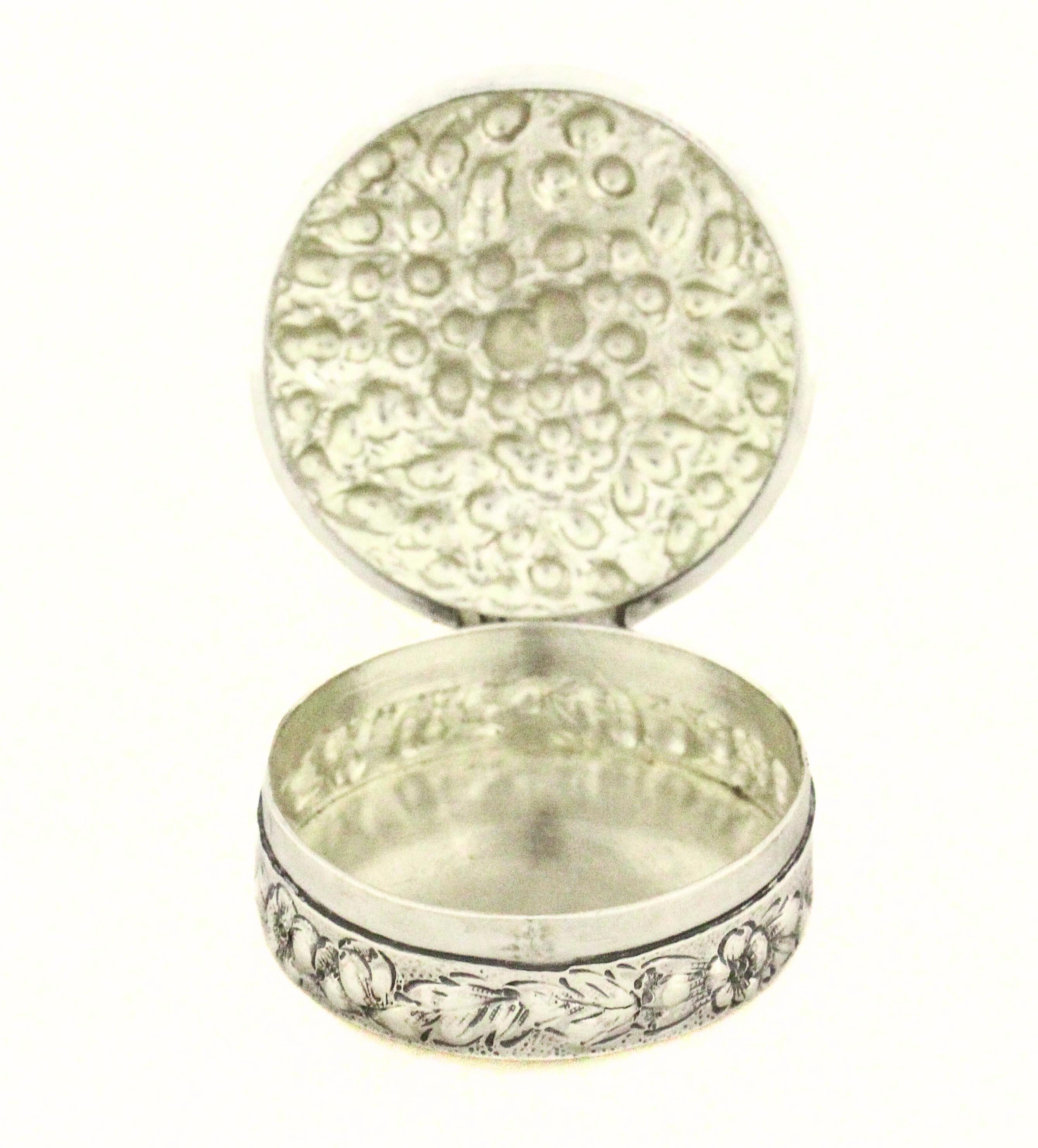 Eine runde Pillendose aus feinem Sterlingsilber von Black, Starr & Frost, mit einem Durchmesser von etwa 5,1 cm (2 Zoll). Der Deckel der Dose ist mit einem Repoussé-Dekor versehen, das sorgfältig in Relief gearbeitet ist und Blattmotive und zarte