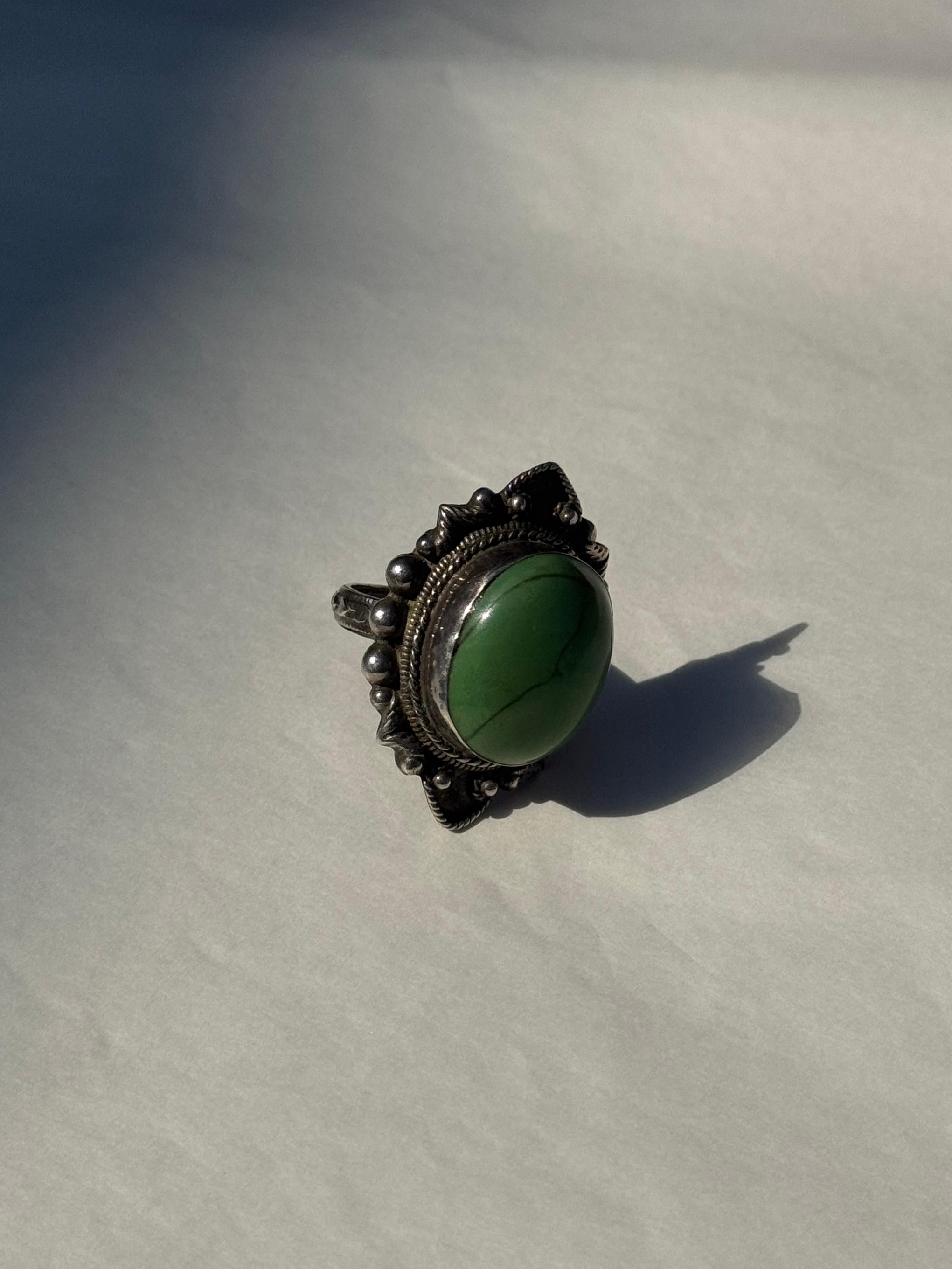 This striking vintage statement ring showcases a generously sized green howlite cabochon, set in a richly decorated sterling silver frame. Crafted circa 1970s, the piece embodies a bold bohemian spirit, blending earthy elegance with intricate