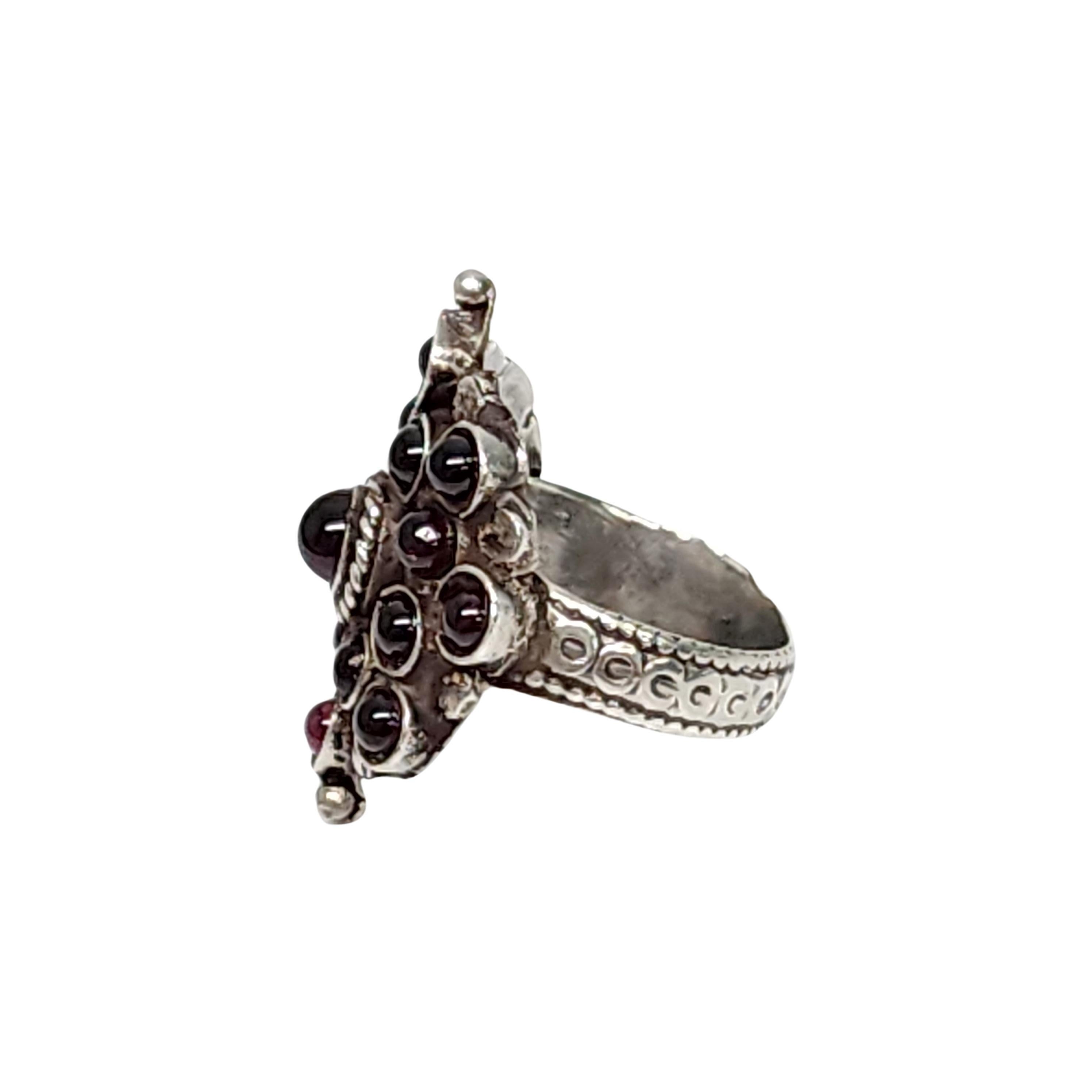 Sterling silver ruby cabochon cluster ring.

Size 6 1/2

Round bezel set ruby cabochon stones surround one slightly larger center stone with rope edge accent. Ornate band.

Measures approx 1 1/8