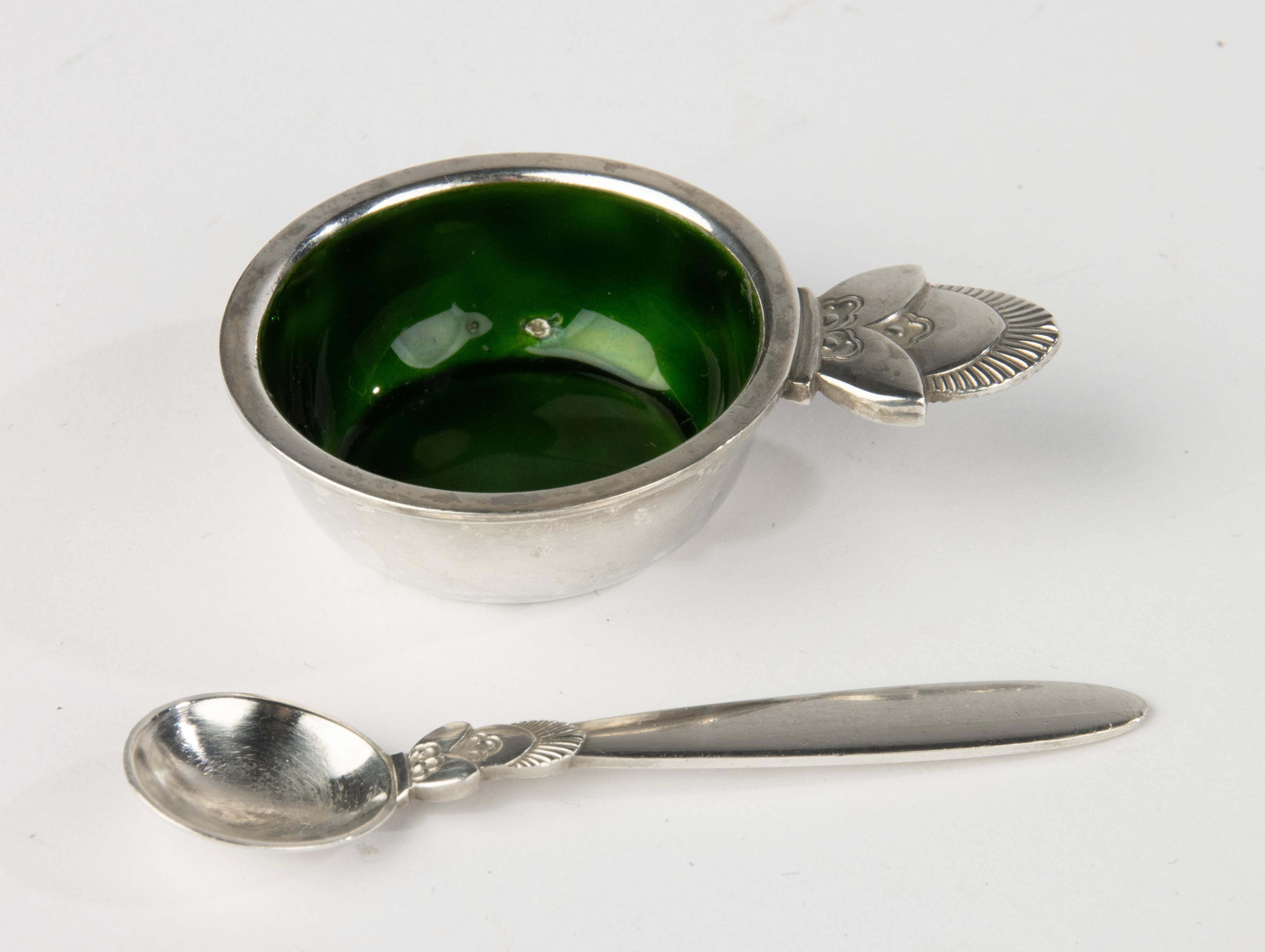 Una hermosa taza de sal de plata con el interior esmaltado. Con ella una pequeña cuchara de sal, originalmente perteneciente a la taza.
Es de plata de ley, fabricado por George Jensen.
La taza de sal está en buen estado, sólo tiene un punto muy