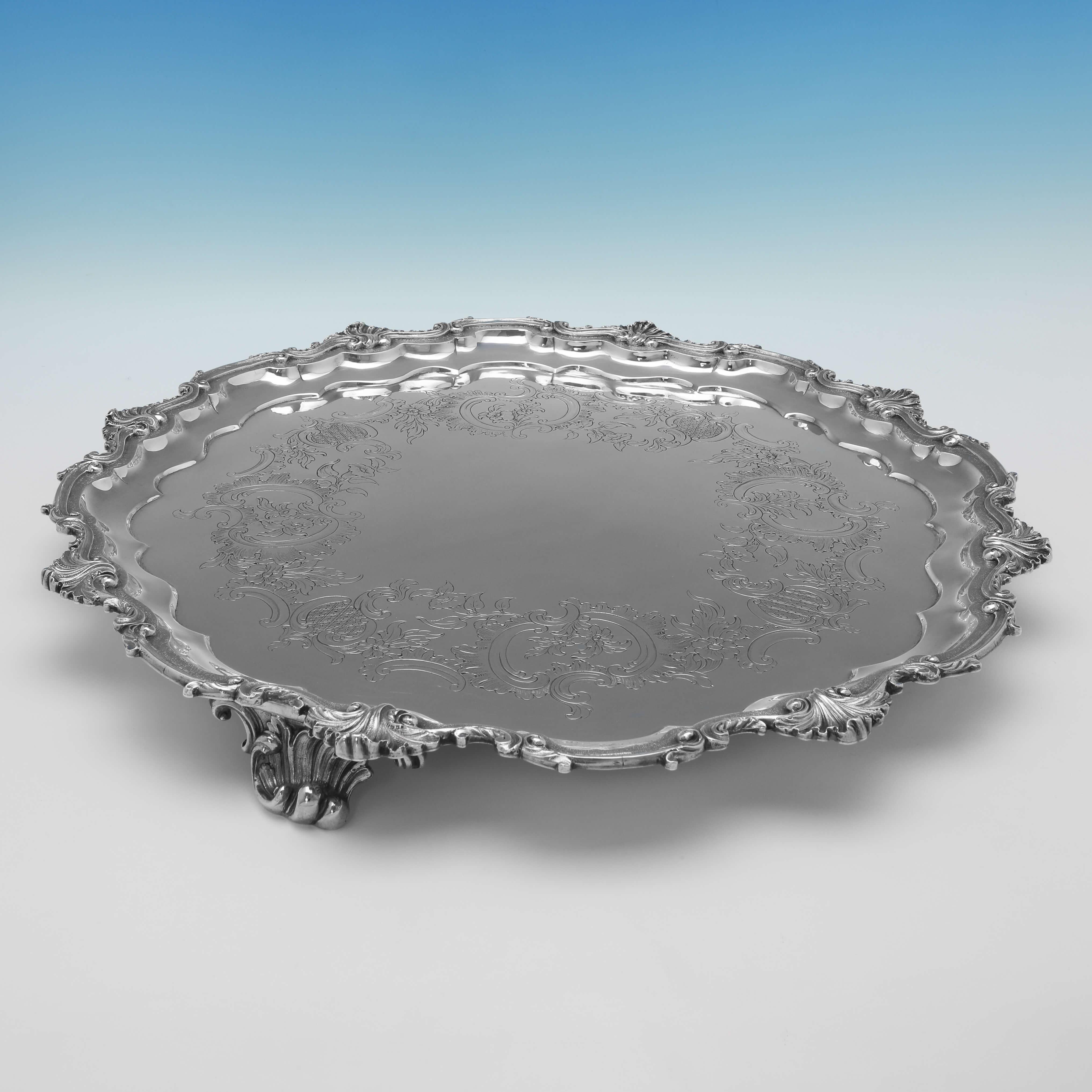 Hallmarked in London in 1844 by Benjamin Smith, this striking, Victorian, Antique Sterling Silver Salver, features a shell and scroll border, engraved decoration, and stands on three scroll feet. The salver measures 20