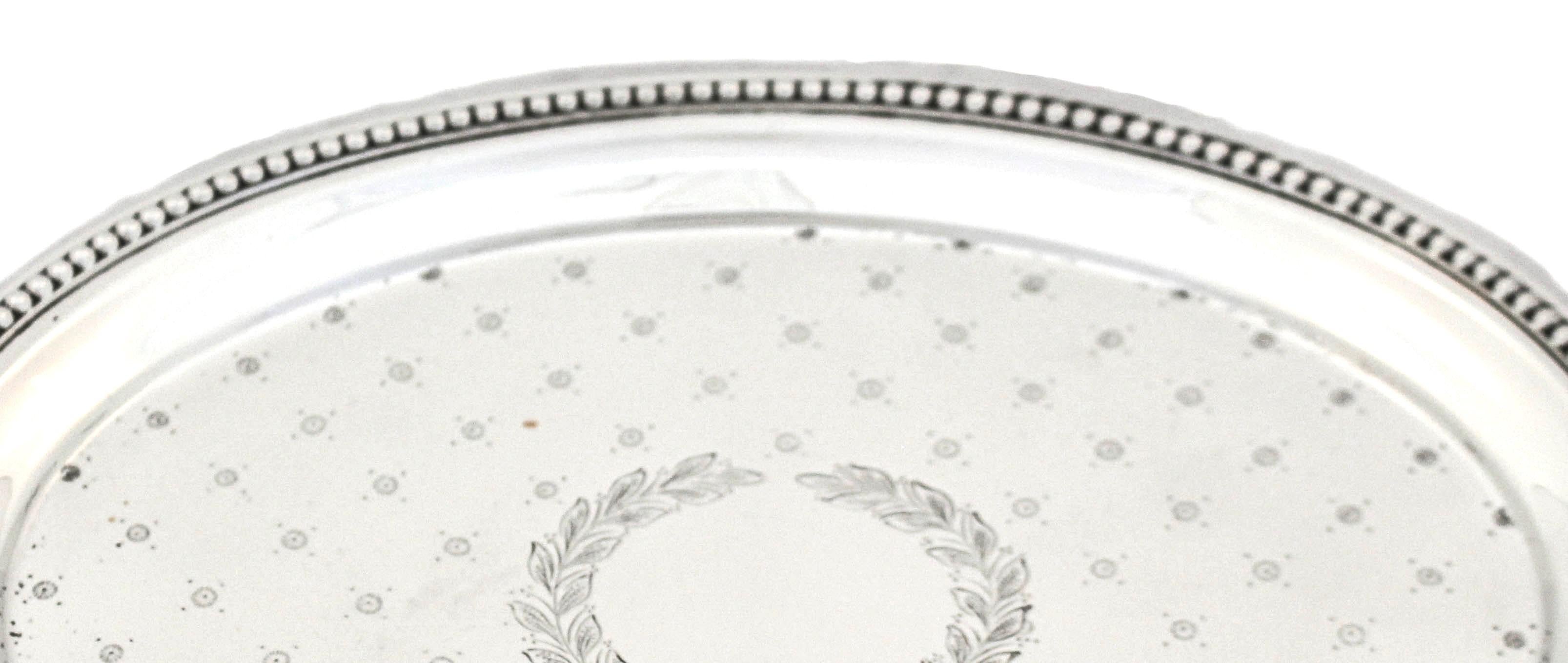 Being offered is a sterling silver salver by J. E. Caldwell of Philadelphia. 
This lovely antique piece is oval shaped and has a row of beads going around the edge.  It stands on four feet so it is raised off the surface.  In the center a wreath
