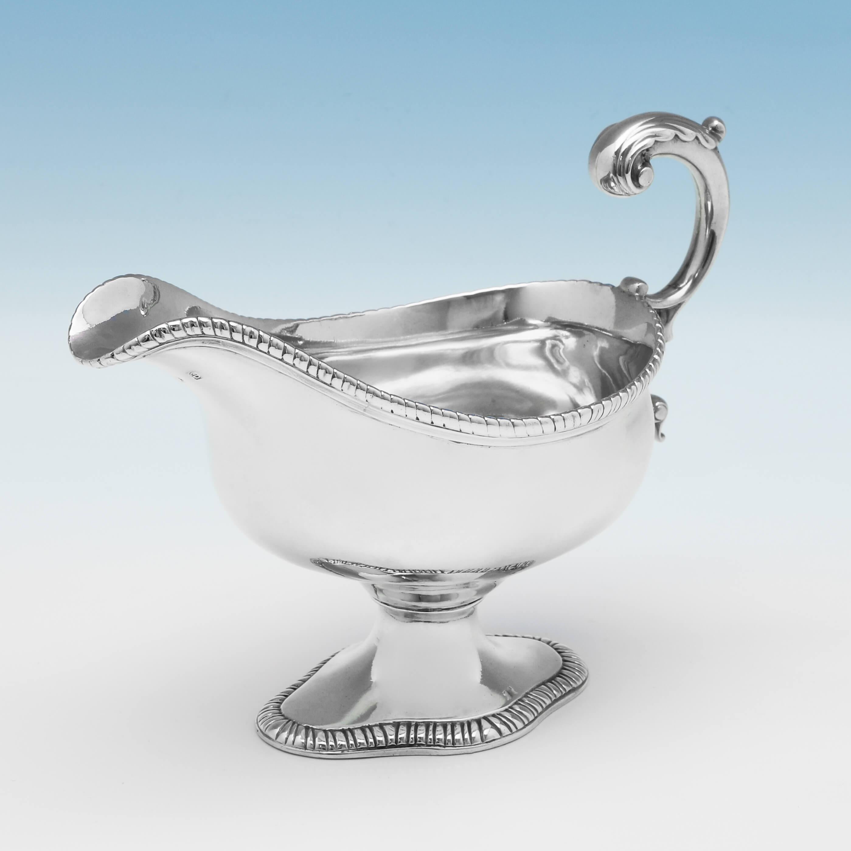Hallmarked in London in 1780, this handsome, George III, antique sterling silver sauce boat, is plain in style, standing on a pedestal foot, and featuring gadroon borders, and an acanthus detailed flying C-scroll handle. The sauce boat measures 5
