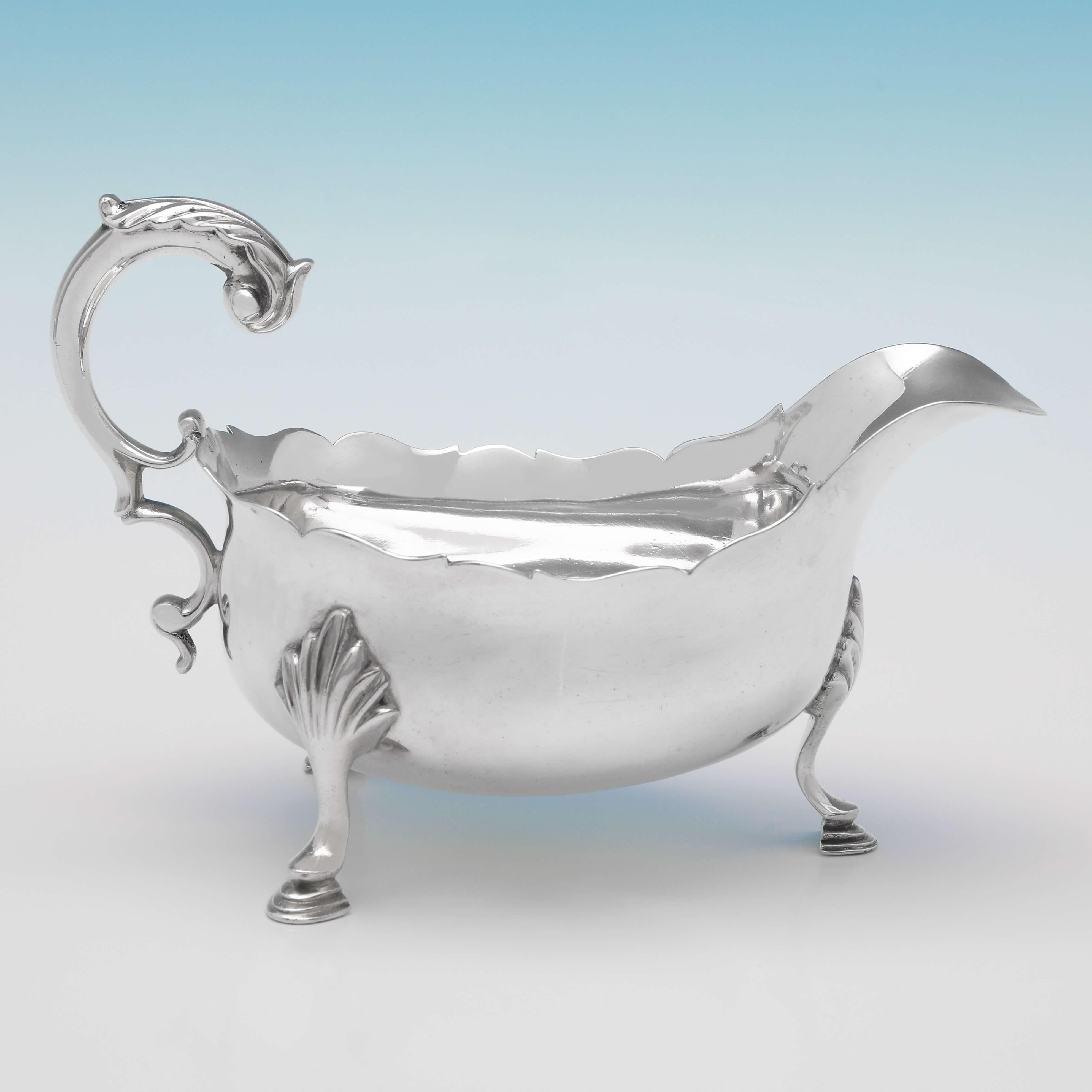 Hallmarked in London in 1781, this handsome, George III, Antique Sterling Silver Sauce Boat, features a shaped border, an acanthus detailed flying scroll handle, and stands on three hoof feet. The sauce boat measures 4.25