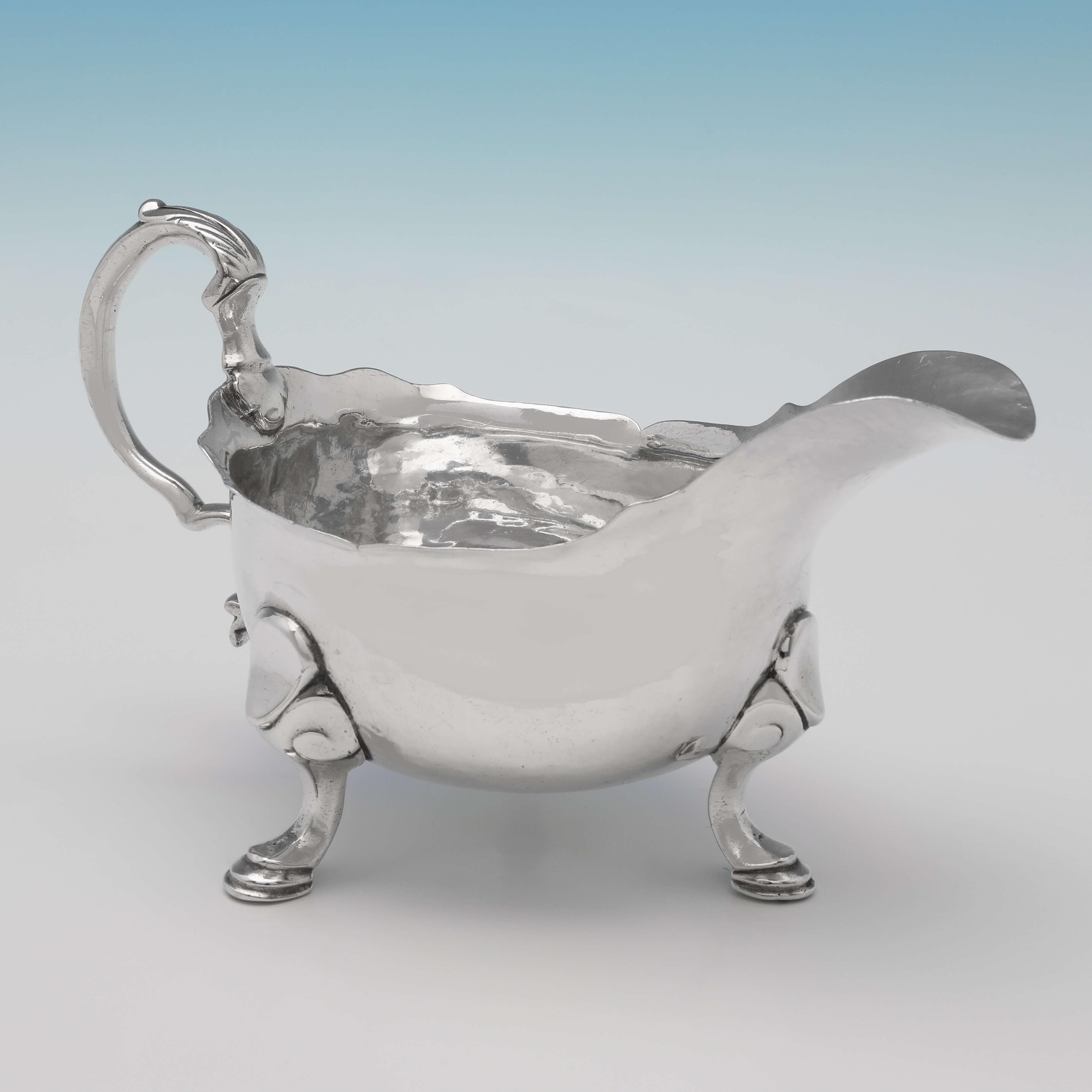 Hallmarked in London in 1750, this handsome, George II, Antique Sterling Silver Sauce Boat, features a shaped border, an acanthus detailed handle, an engraved crest to one side, and stands on three feet. The sauce boat measures 4.25