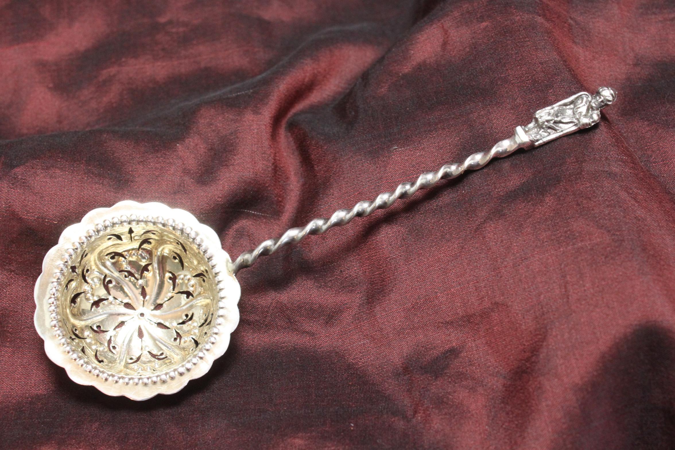 This very decorative sterling silver sifter spoon was made by Charles Harris in London in 1889.  On top of the barley twist handle is a cast silver figure of a man in a Middle Eastern cloak and turban who is holding a staff. The bowl has been very