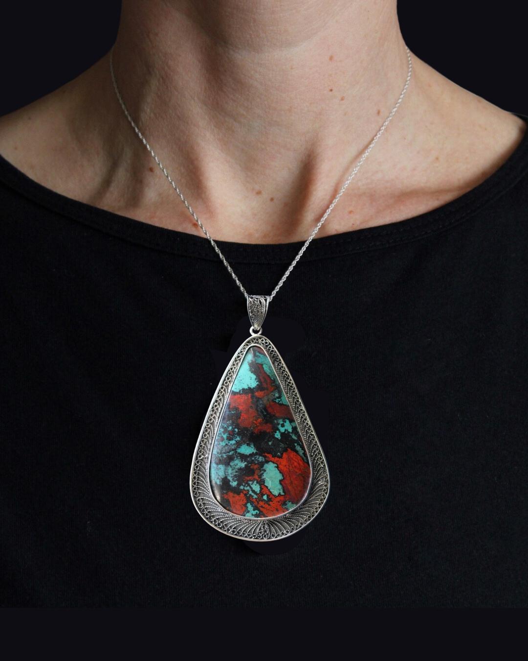This pendant features a dramatic Sonoran Sunset cabochon. Sonoran Sunset (also known as Sonora Sunrise) is from the Milpillas Mine in Sonora, Mexico and is comprised of three different stones; the blue/green comes from Chrysocolla, the red from