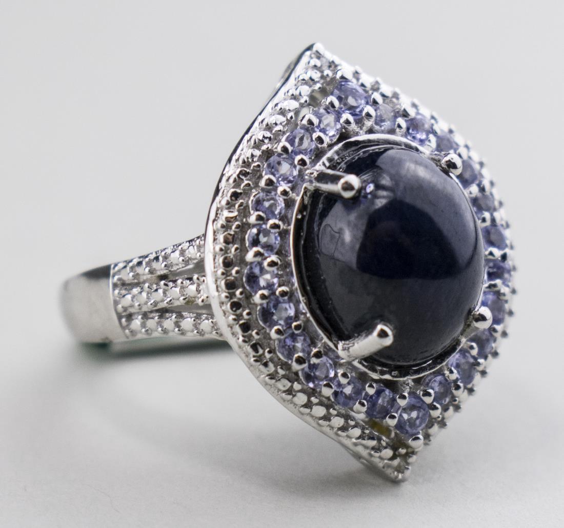 Sterling silver ring with a central oval star sapphire cabochon accented with light blue stones. Size 7 3/4.