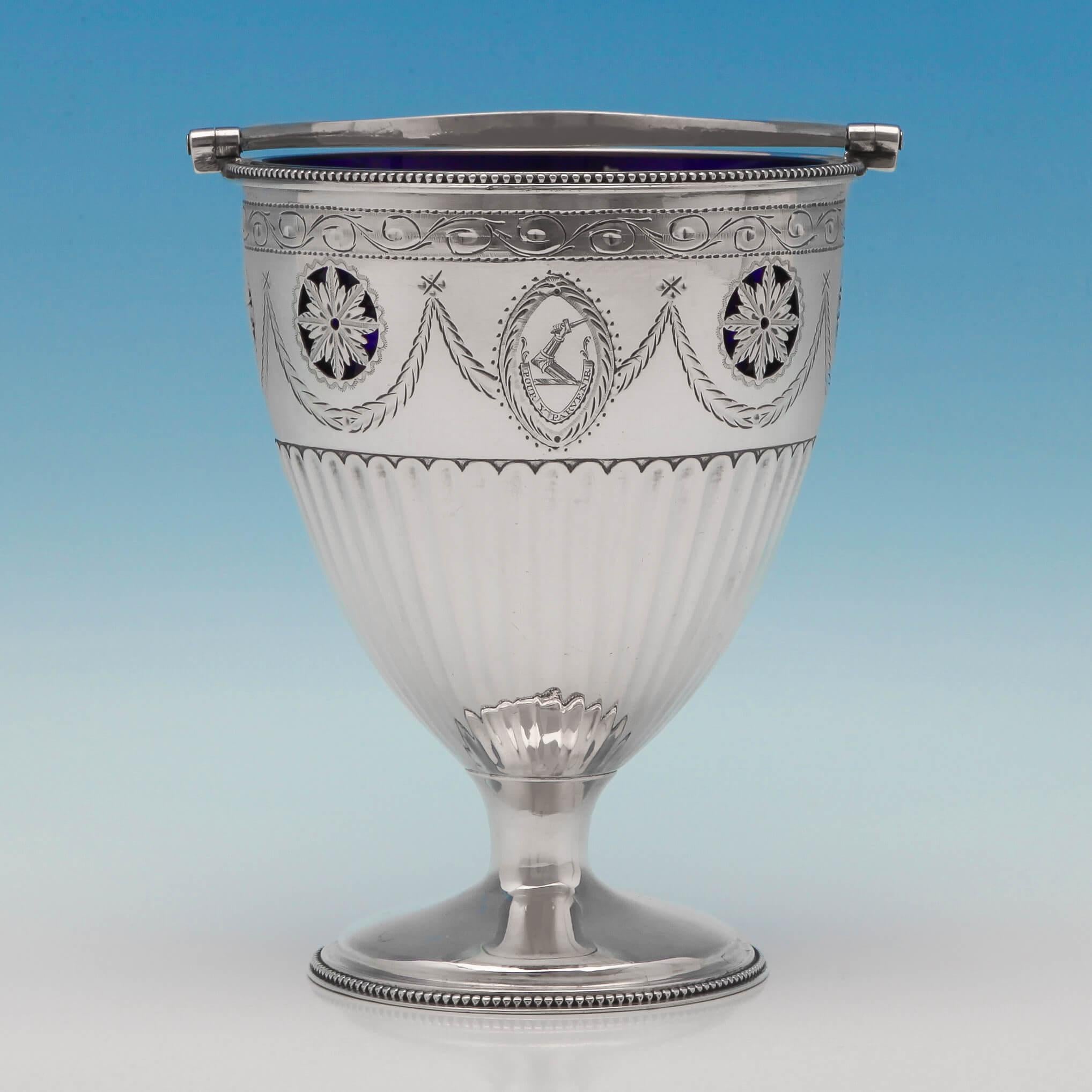 Hallmarked in London in 1783 by Barrage Davenport, this delightful, George III, antique, sterling silver sugar basket, has a half fluted body with bead borders, a blue glass liner and a beaded swing handle. Featuring pretty pierced floral motifs