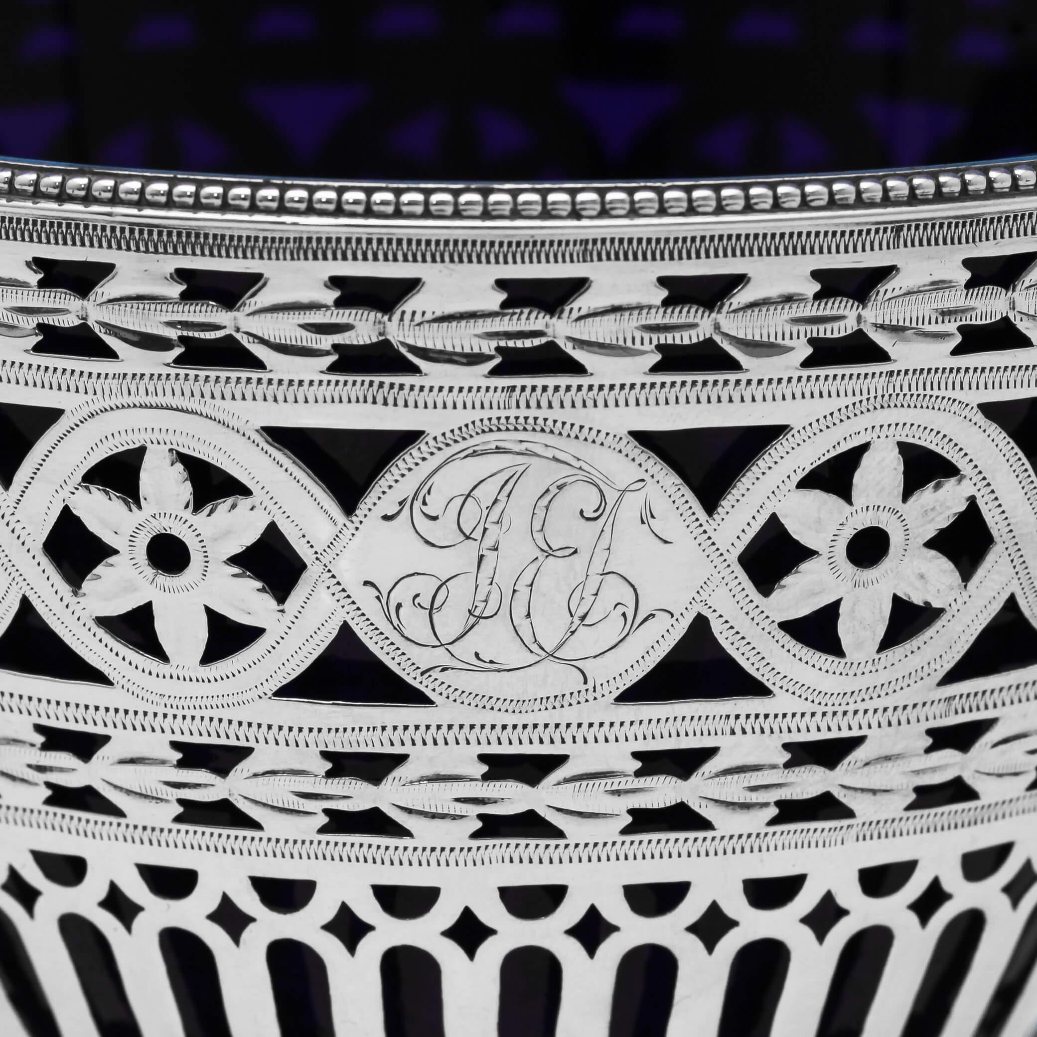 Hallmarked in London in 1781 by Robert Hennell I, this striking, George III, antique sterling silver sugar basket, features pierce and engraved decoration, bead borders and a blue glass liner. The central cartouche is engraved with a monogram. The