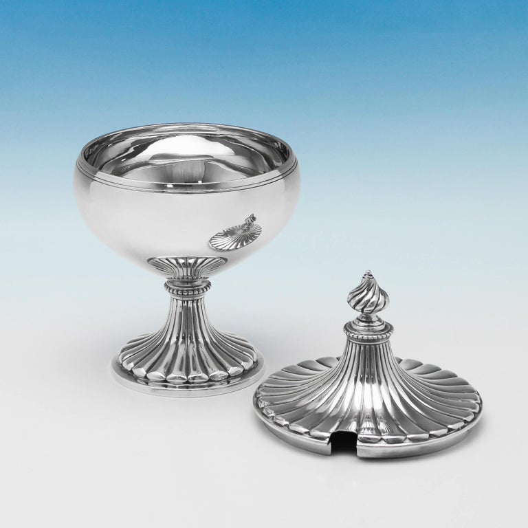 Hallmarked in London in 1910 by Holland, Aldwinckle & Slater, this elegant, George V, antique, sterling silver sugar bowl, features fluted decoration to the foot and lid, and a hole for a spoon. The sugar bowl measures 6.5