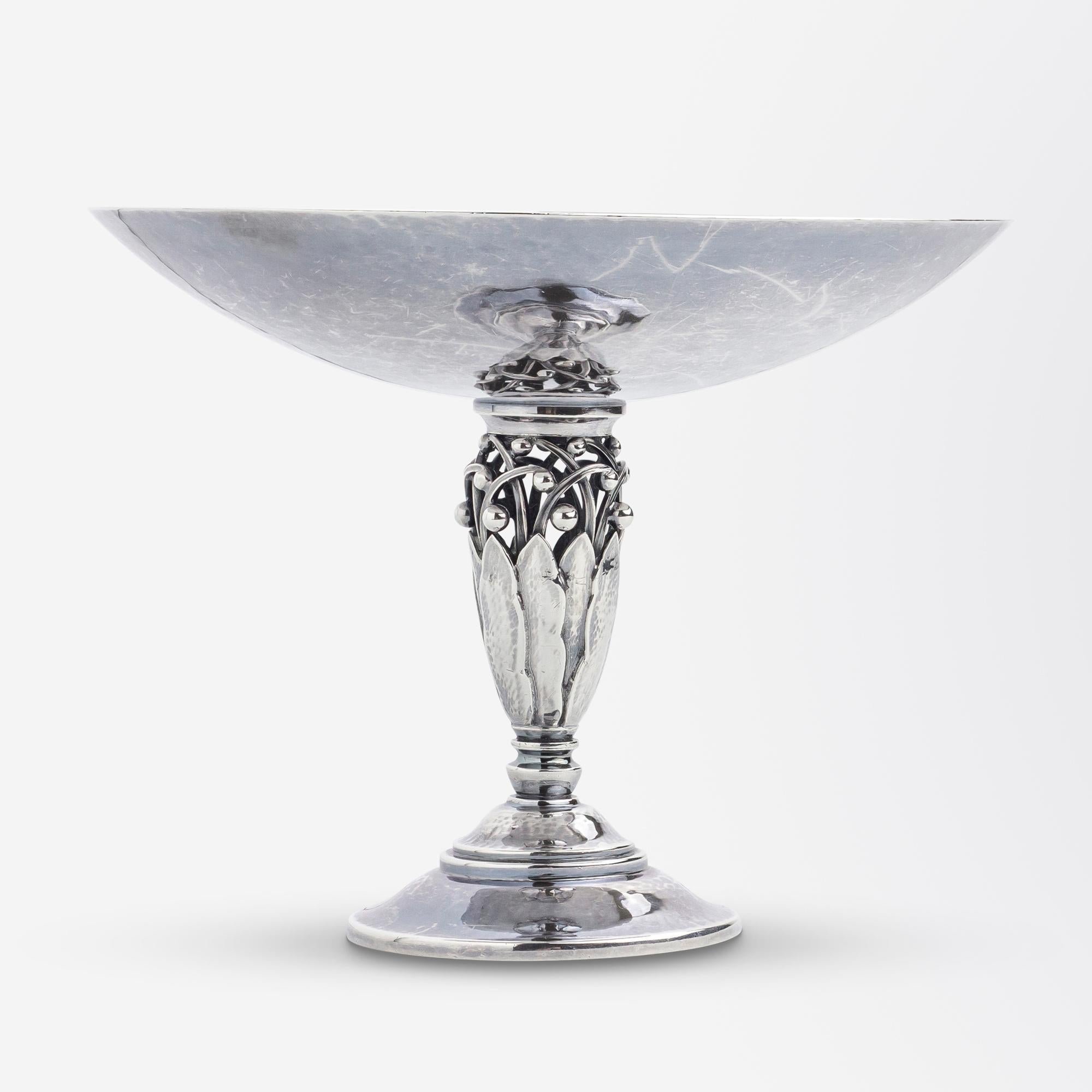 This really charming tazza or 'footed comport' was crafted by Georg Jensen in a design first conceived by Johan Rohde (1856-1935) known as pattern '574C'. The piece features a shallow bowl to the top which is supported by an openwork stylised leaf